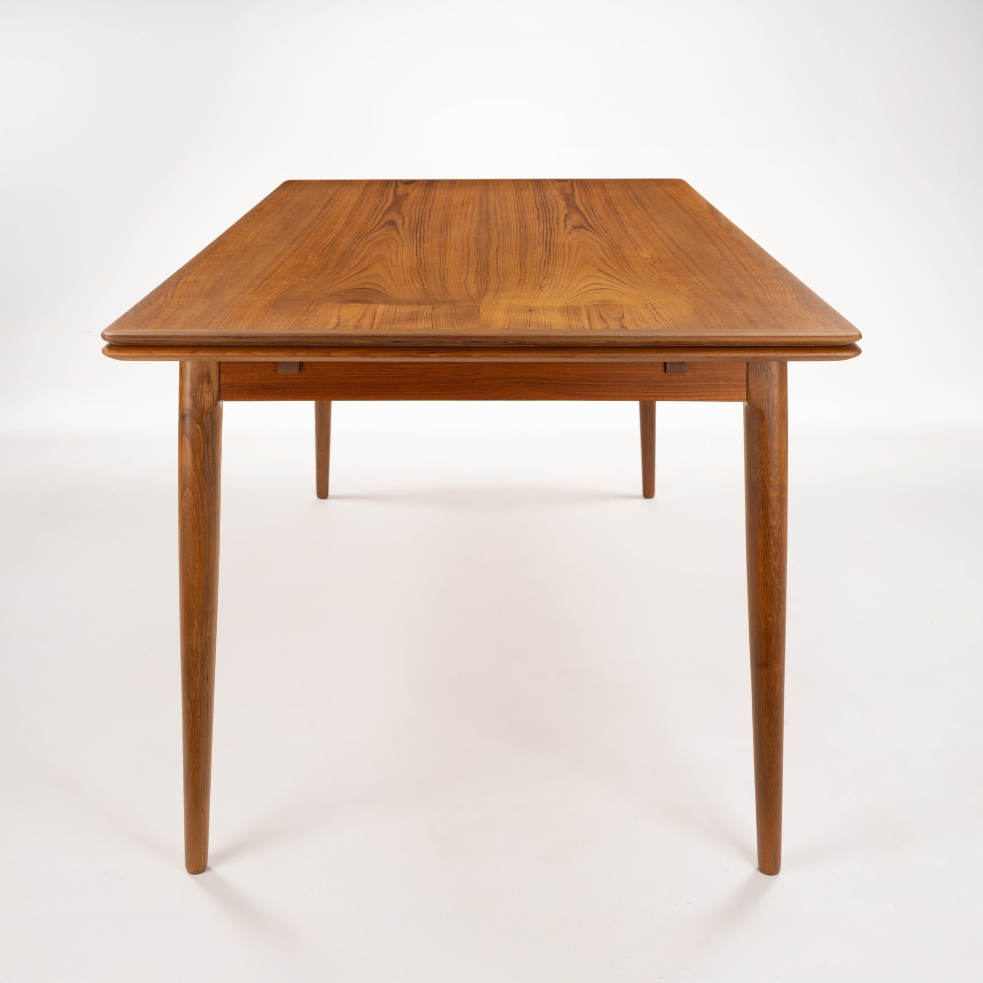 Danish Draw-Leaf Dining Table in Teak featuring rich wood grain a rounded rectangular top and elegant tapered legs in vintage Danish furniture style