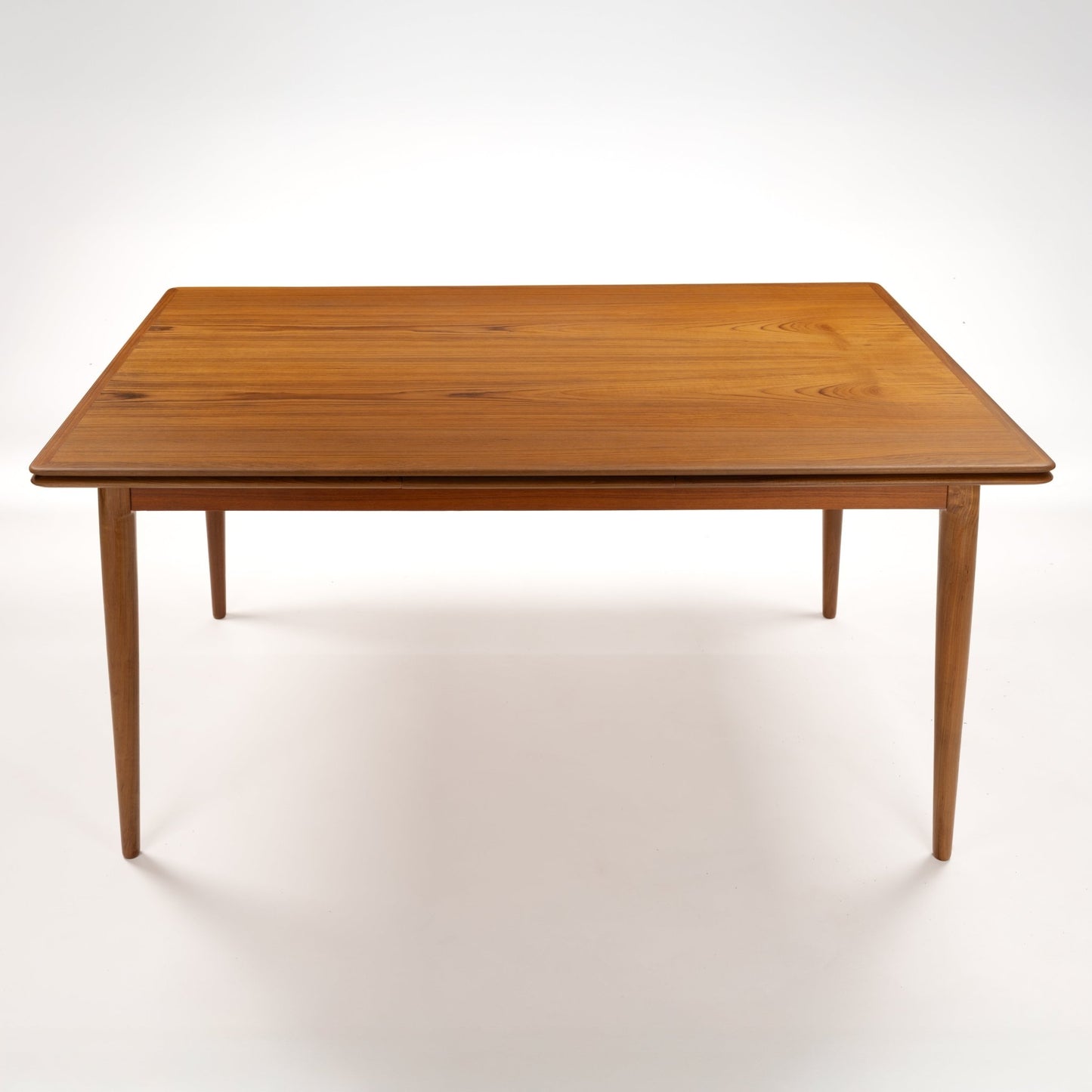 Danish Draw-Leaf Dining Table in Teak with warm linear wood grain a rectangular top and four slender tapered legs in vintage Danish furniture style
