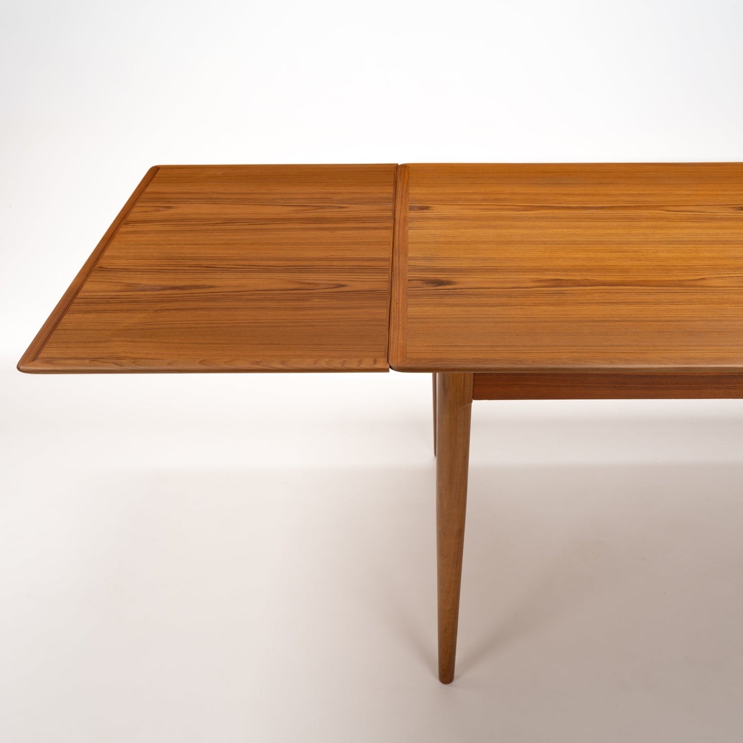 Danish Draw-Leaf Dining Table in Teak with rich linear wood grain a recessed edge and tapered leg showcasing vintage Danish furniture craftsmanship