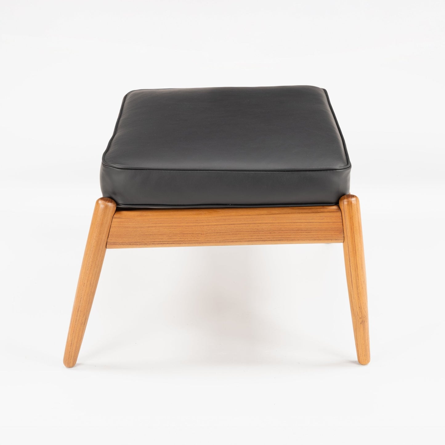 Danish Teak Ottoman with Black Leather featuring a soft black leather cushion on a light teak frame with angled legs, capturing timeless mid century modern seating design.