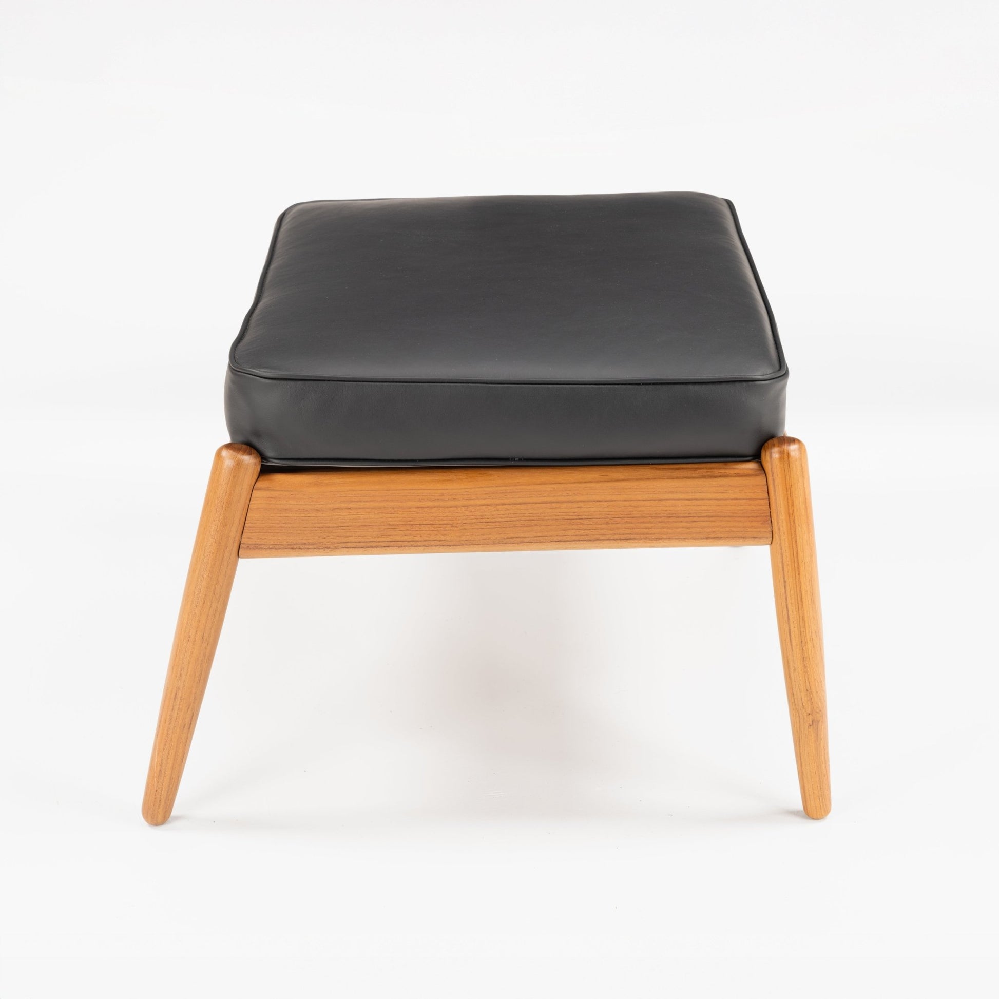 Danish Teak Ottoman with Black Leather featuring a soft black leather cushion on a light teak frame with angled legs, capturing timeless mid century modern seating design.