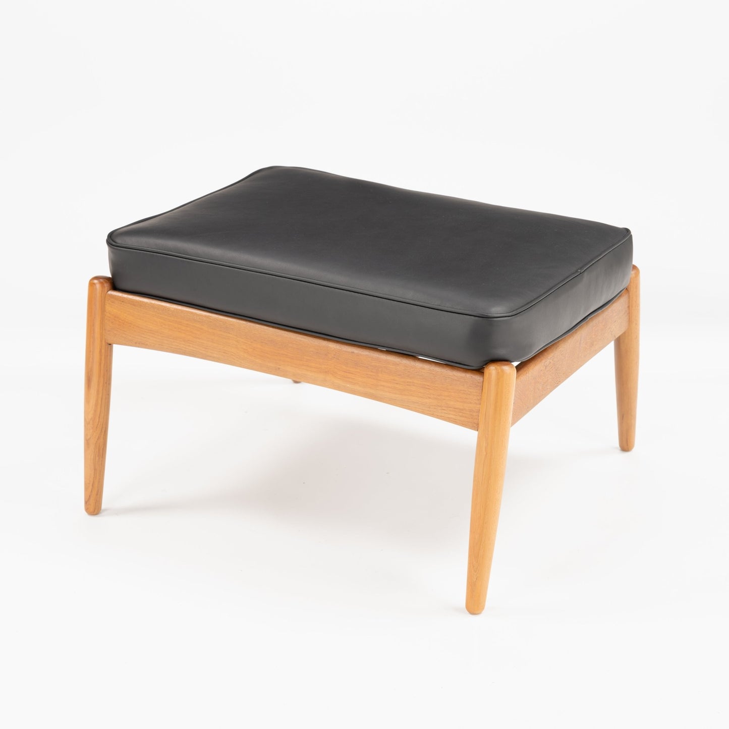 Danish Teak Ottoman with Black Leather showcasing a cushioned black leather top resting on a warm teak frame with gently tapered legs, reflecting classic mid century modern seating style.