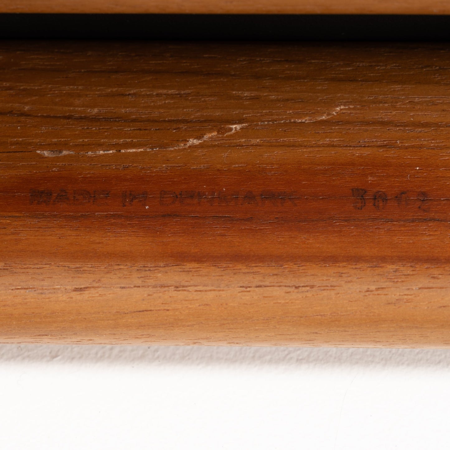 Close-up of a warm-toned teak wood frame with subtle engraved text, highlighting craftsmanship details of the Danish Teak Ottoman with Black Leather.