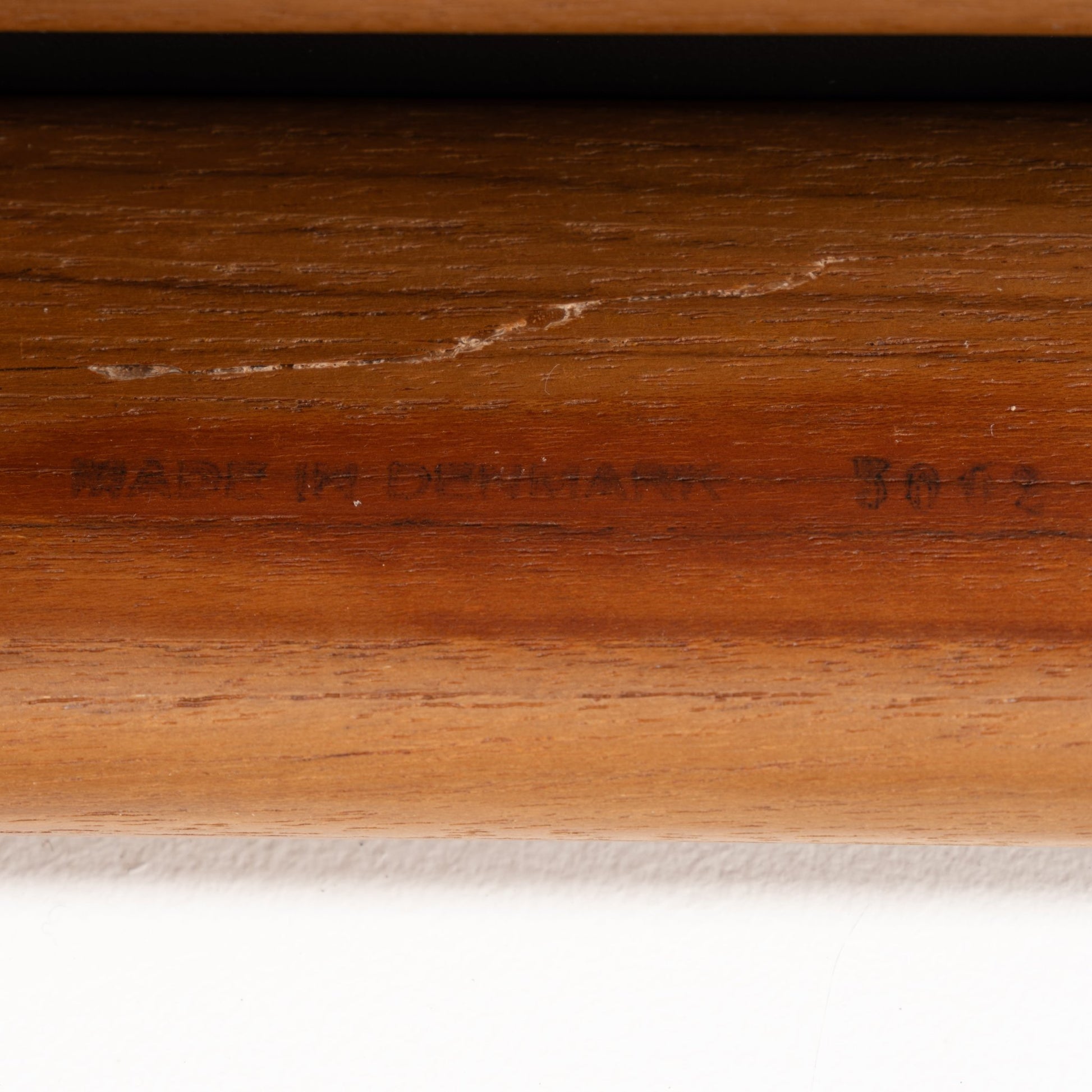 Close-up of a warm-toned teak wood frame with subtle engraved text, highlighting craftsmanship details of the Danish Teak Ottoman with Black Leather.