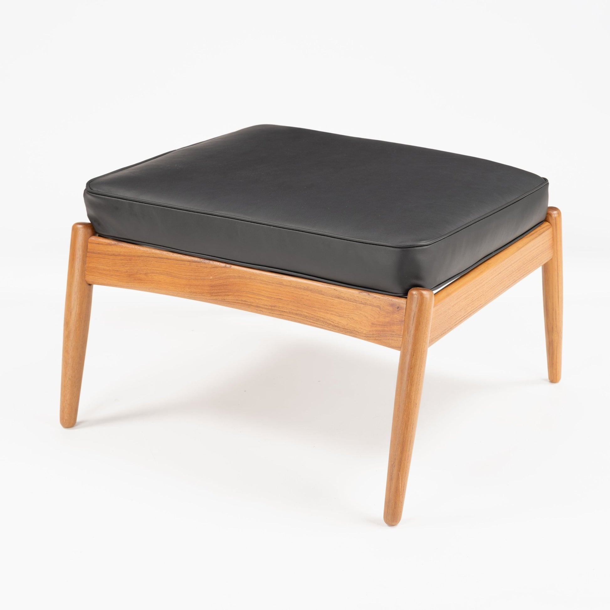 Danish Teak Ottoman with Black Leather featuring a plush black leather cushion atop a sleek teak frame with gently tapered legs, exemplifying vintage mid century modern seating design.