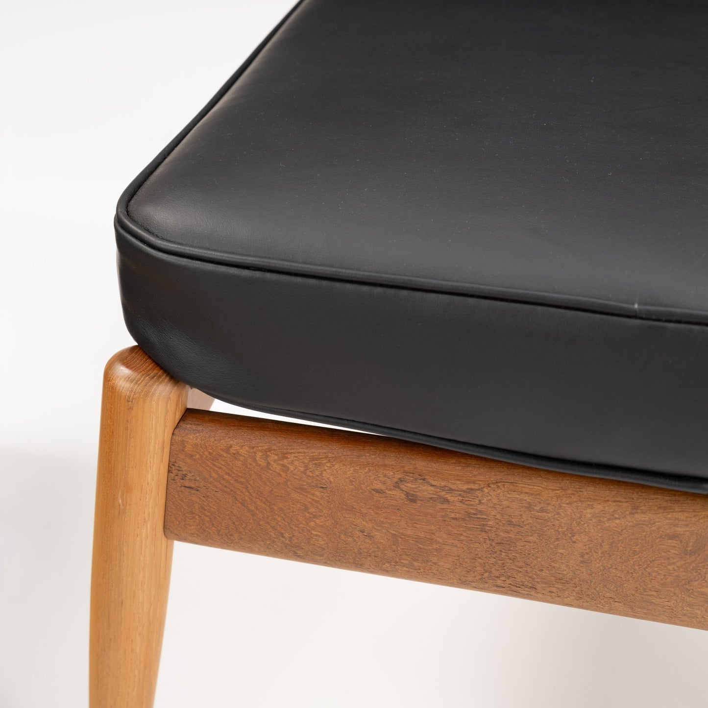 Danish Teak Ottoman with Black Leather featuring a smooth black leather cushion resting on a warm-toned teak frame with rounded legs, exemplifying refined mid century modern seating craftsmanship.
