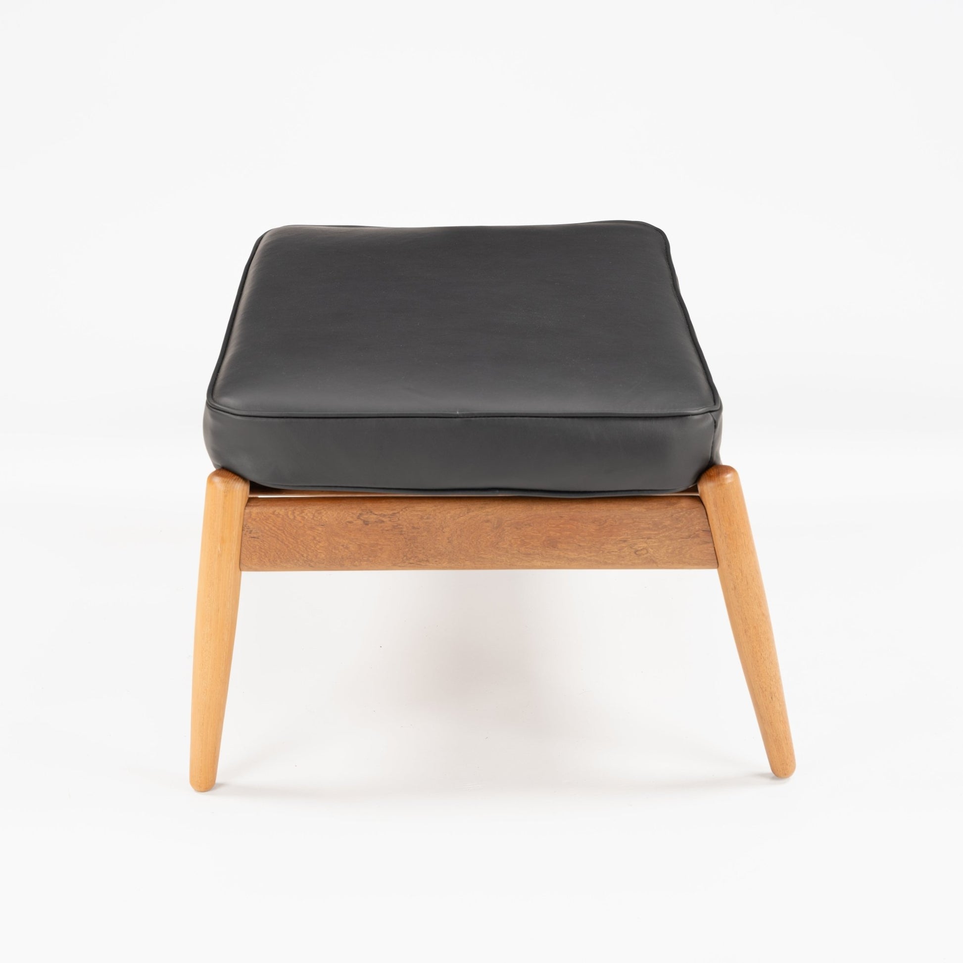 Danish Teak Ottoman with Black Leather showing a smooth black leather cushion atop a warm teak frame with tapered legs, exemplifying elegant mid century modern seating design.