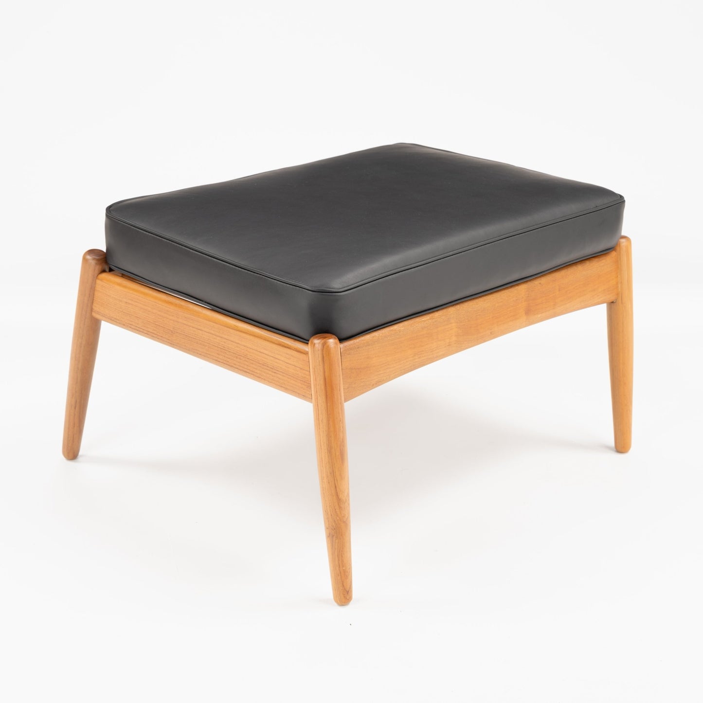 Danish Teak Ottoman with Black Leather featuring a smooth black leather cushion resting on a sleek teak frame with tapered legs, embodying mid century modern seating design.
