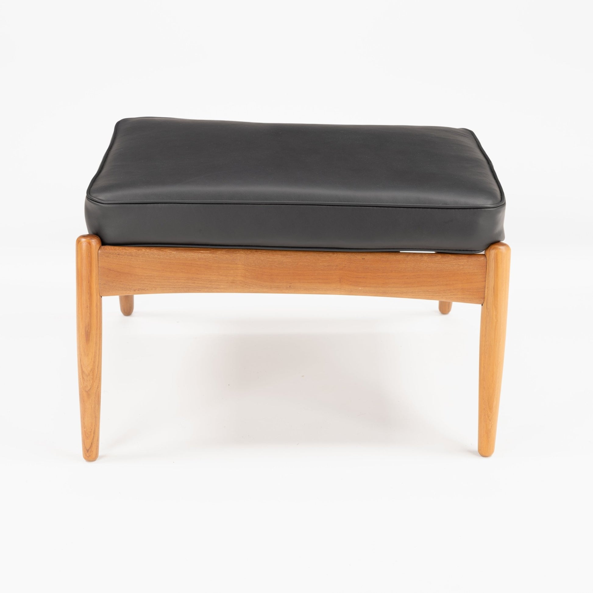 Danish Teak Ottoman with Black Leather displaying a smooth black leather cushion resting atop a warm teak frame with gently tapered legs, embodying refined mid century modern seating design.