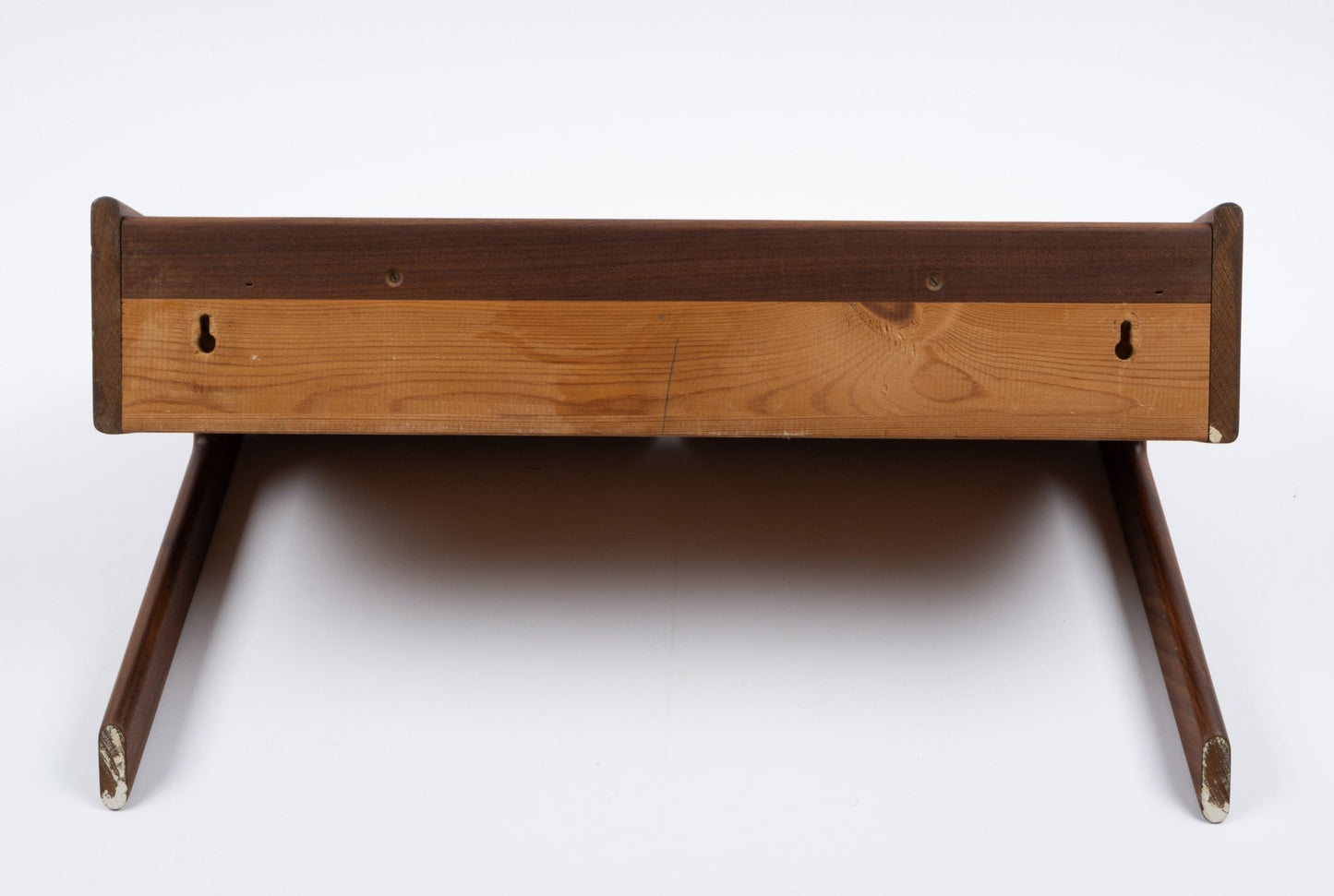 Danish modern teak shelf with drawer, wall-mount hooks, and angled legs, shown from bottom view on white background.