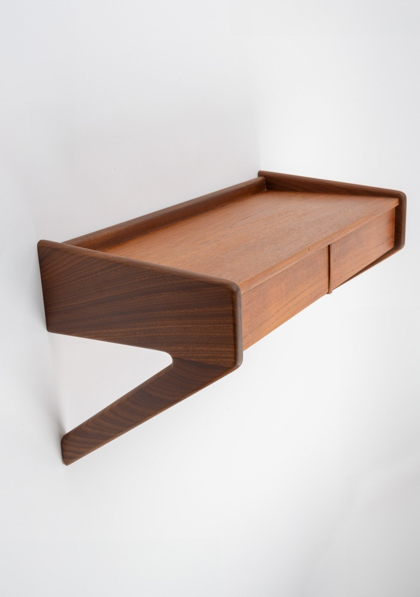 Danish modern teak wall-mounted shelf with integrated drawer and sculptural angled supports in warm wood tone.
