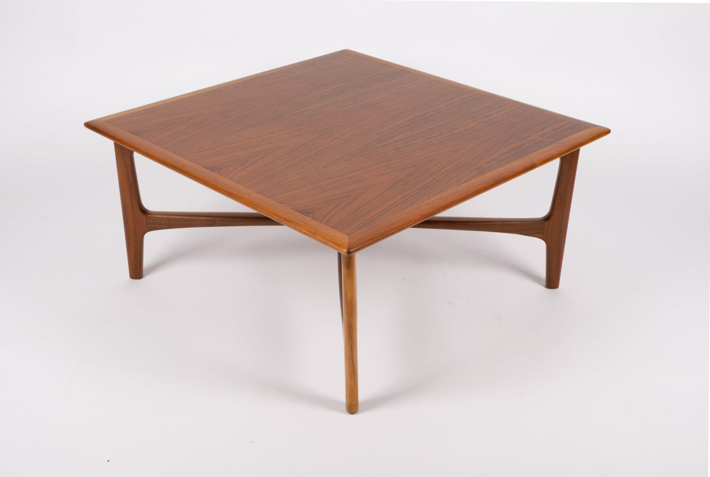 Square mid-century modern teak coffee table with bookmatched top and sculptural x-base design on white background.