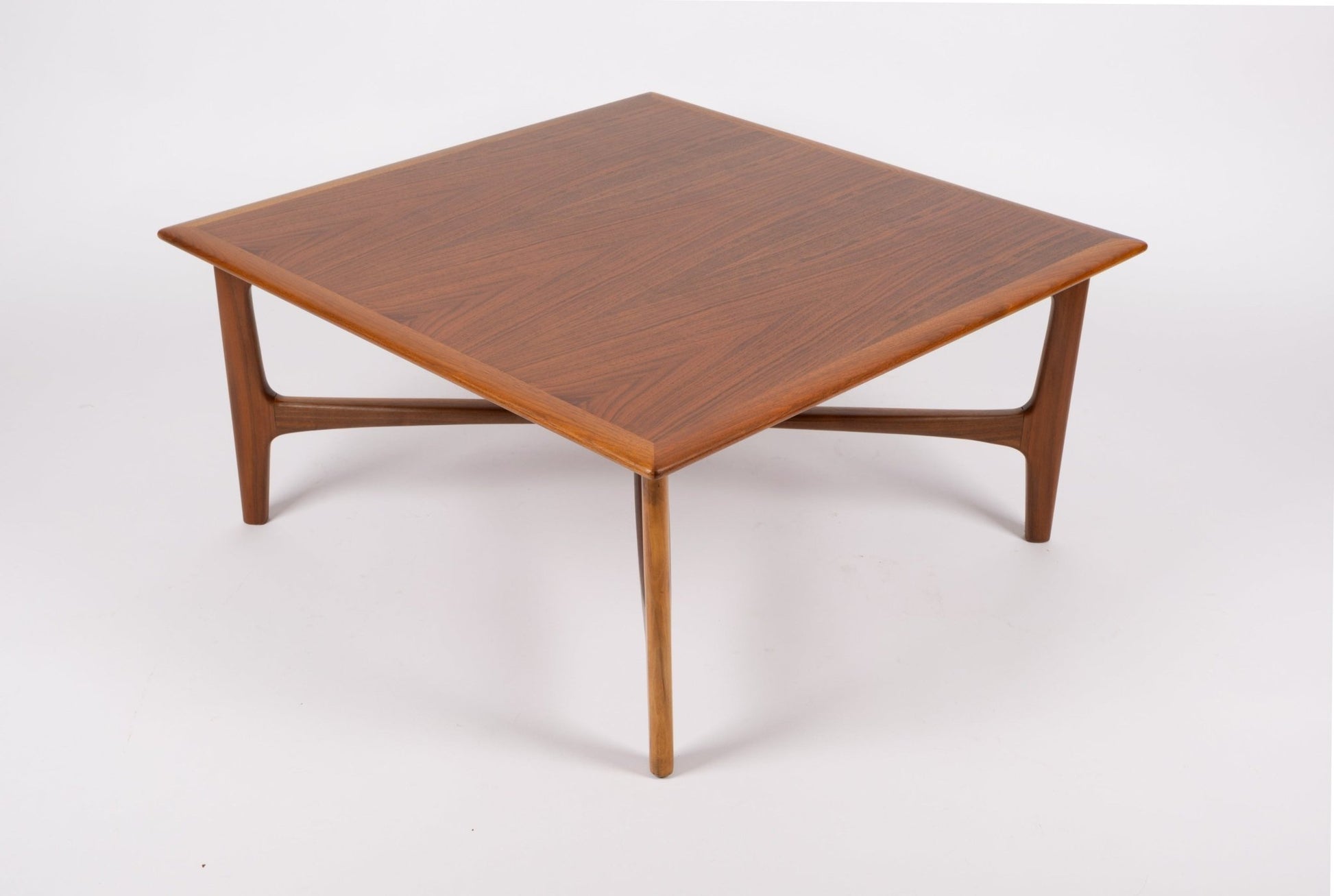 Square mid-century modern teak coffee table with bookmatched top and sculptural x-base design on white background.