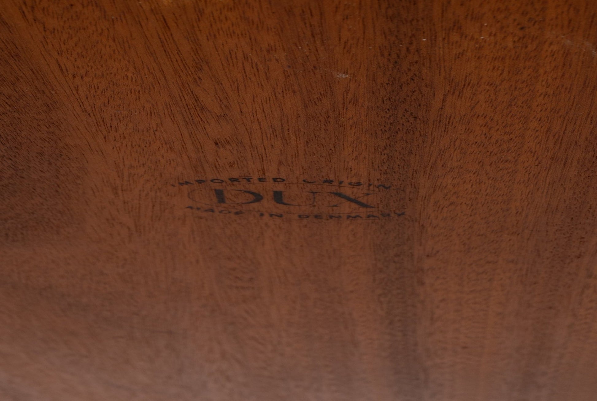 Close-up of stamped DUX logo on the underside of a teak coffee table showcasing wood grain detail.