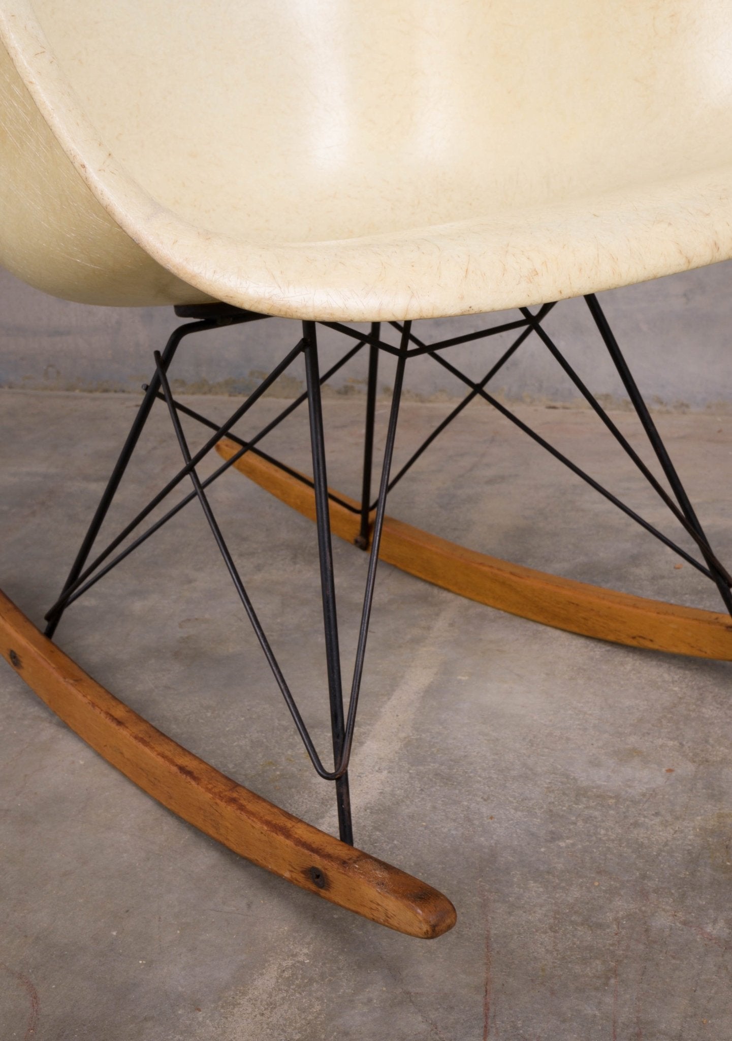 Close-up of Eames Rope-Edge fiberglass rocker with wire base and worn wooden rockers on concrete floor.