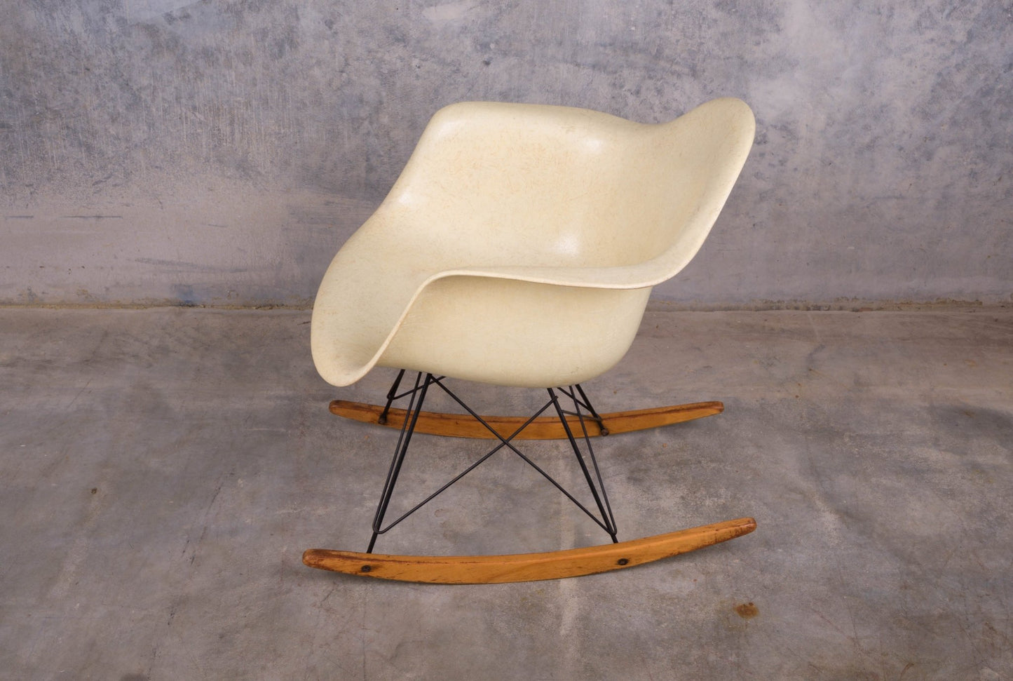 Eames rope-edge fiberglass rocking chair with original wooden rocker base and black metal frame on concrete floor background