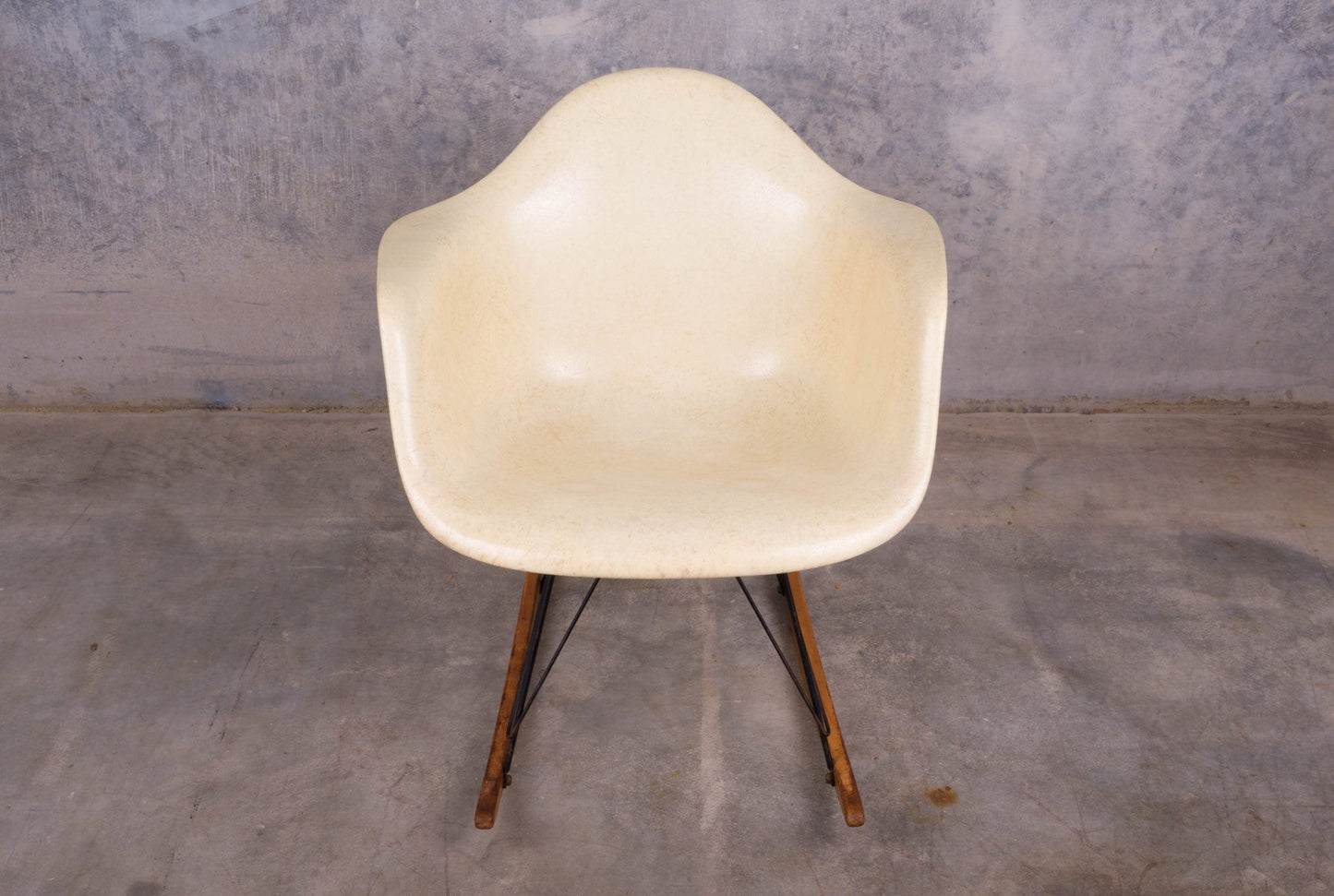 Early production Eames rope-edge fiberglass rocking chair with original wooden rocker base on concrete floor.