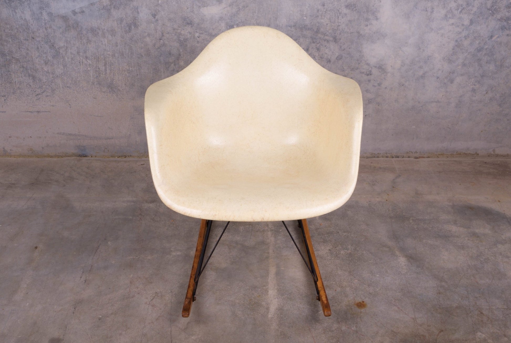 Early production Eames rope-edge fiberglass rocking chair with original wooden rocker base on concrete floor.