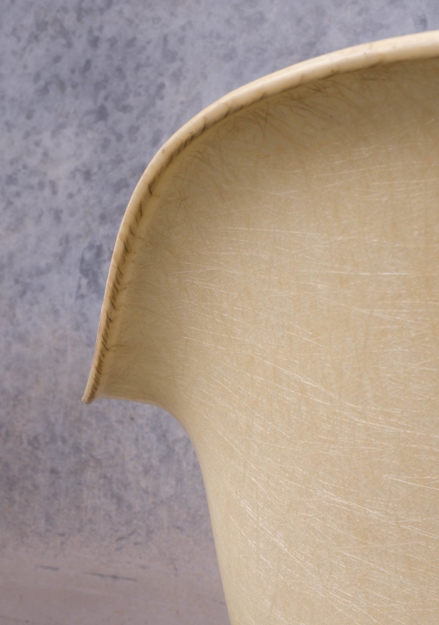 Close-up of vintage Eames rope-edge fiberglass rocking chair shell with textured cream surface and curved edge