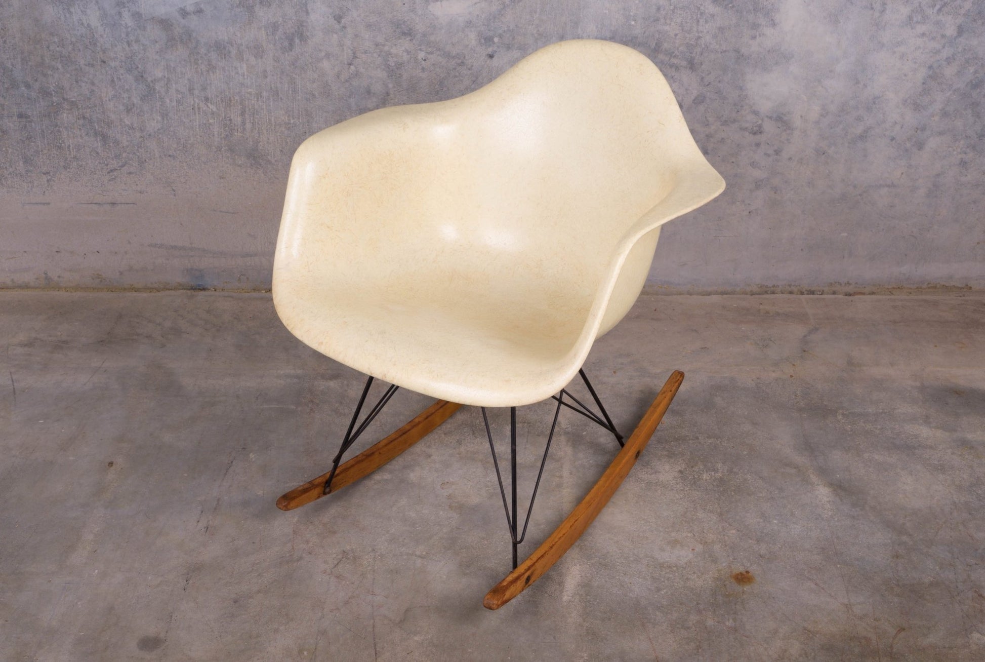 Mid-century modern Eames fiberglass rocking chair with rope edge, metal wire base, and wooden rockers on concrete floor.