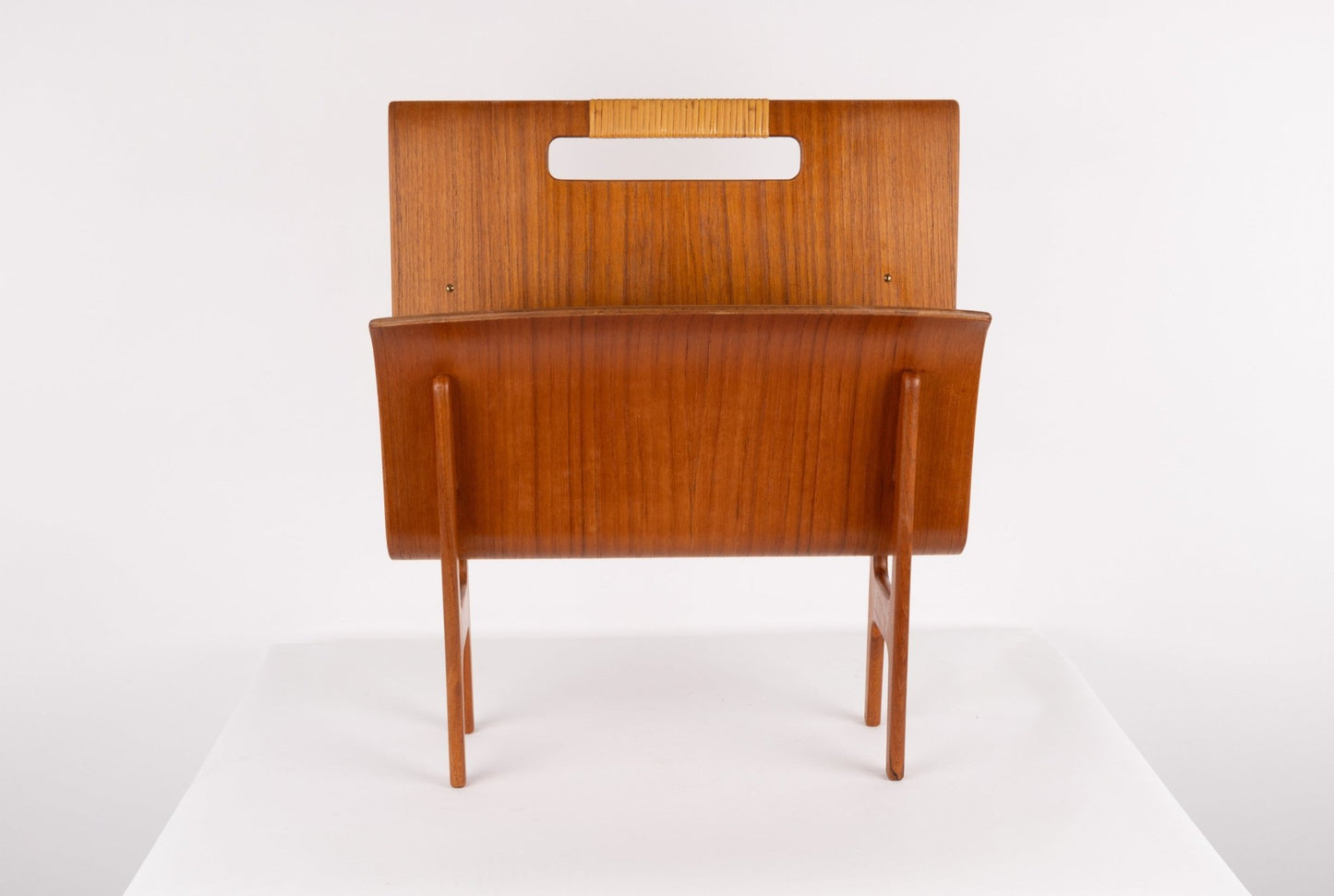 Mid-century modern Ejner Larsen magazine rack in teak with sculpted frame and original cane handle on white background.