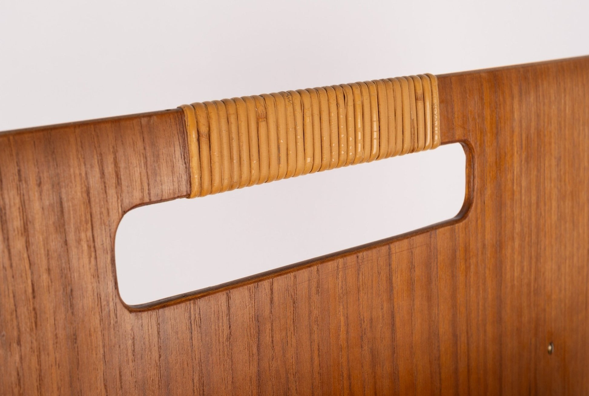 Close-up of mid-century modern teak magazine rack handle wrapped with original cane, highlighting sculpted wood frame detail.