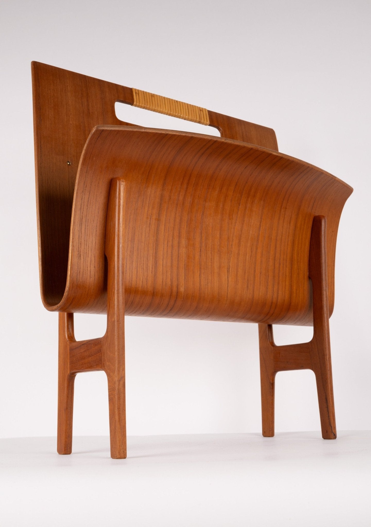 Mid-century modern teak magazine rack with curved molded wood and cane handle on sculpted frame.