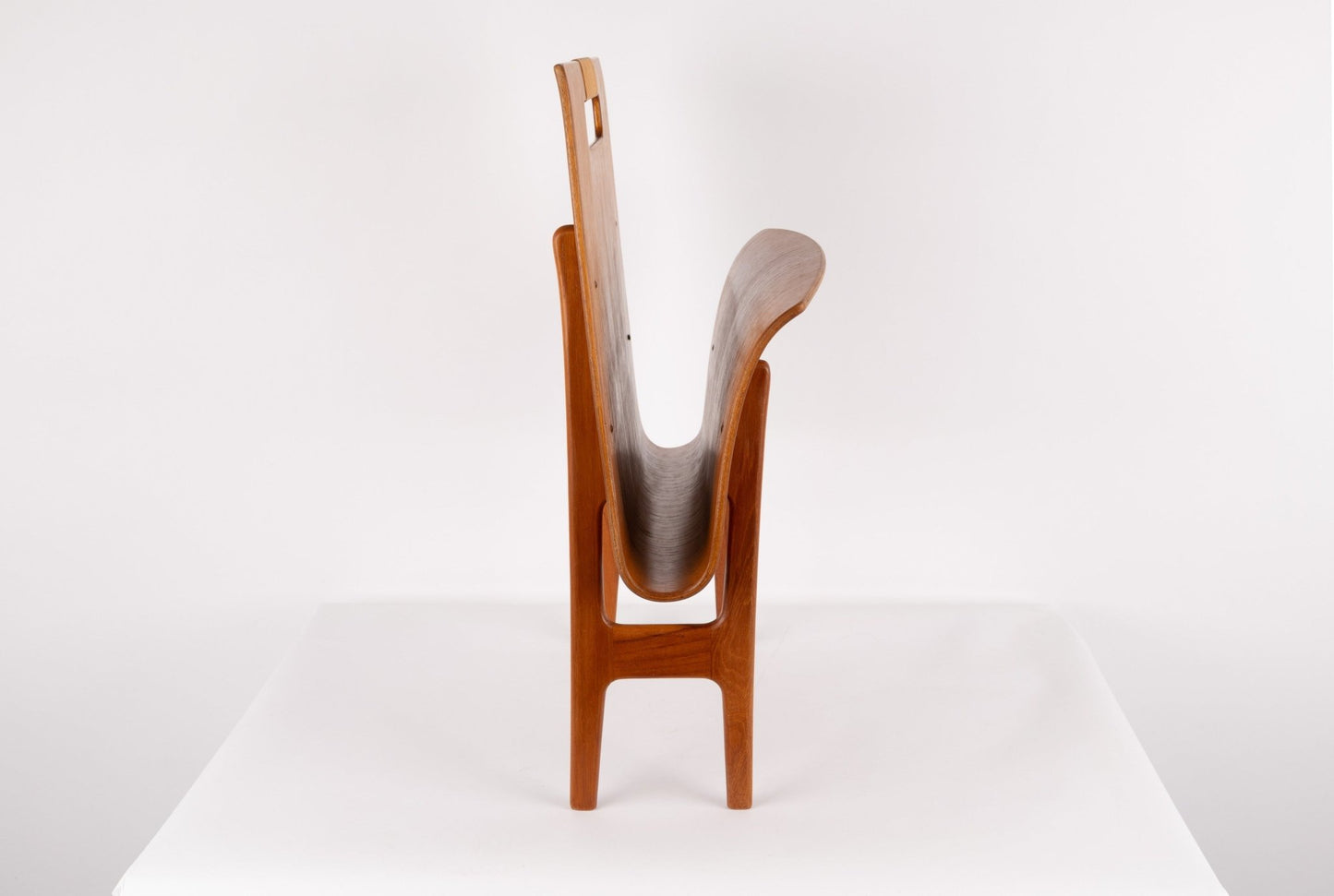 Mid-century modern Ejner Larsen teak magazine rack with sculpted frame and original cane handle on white background.