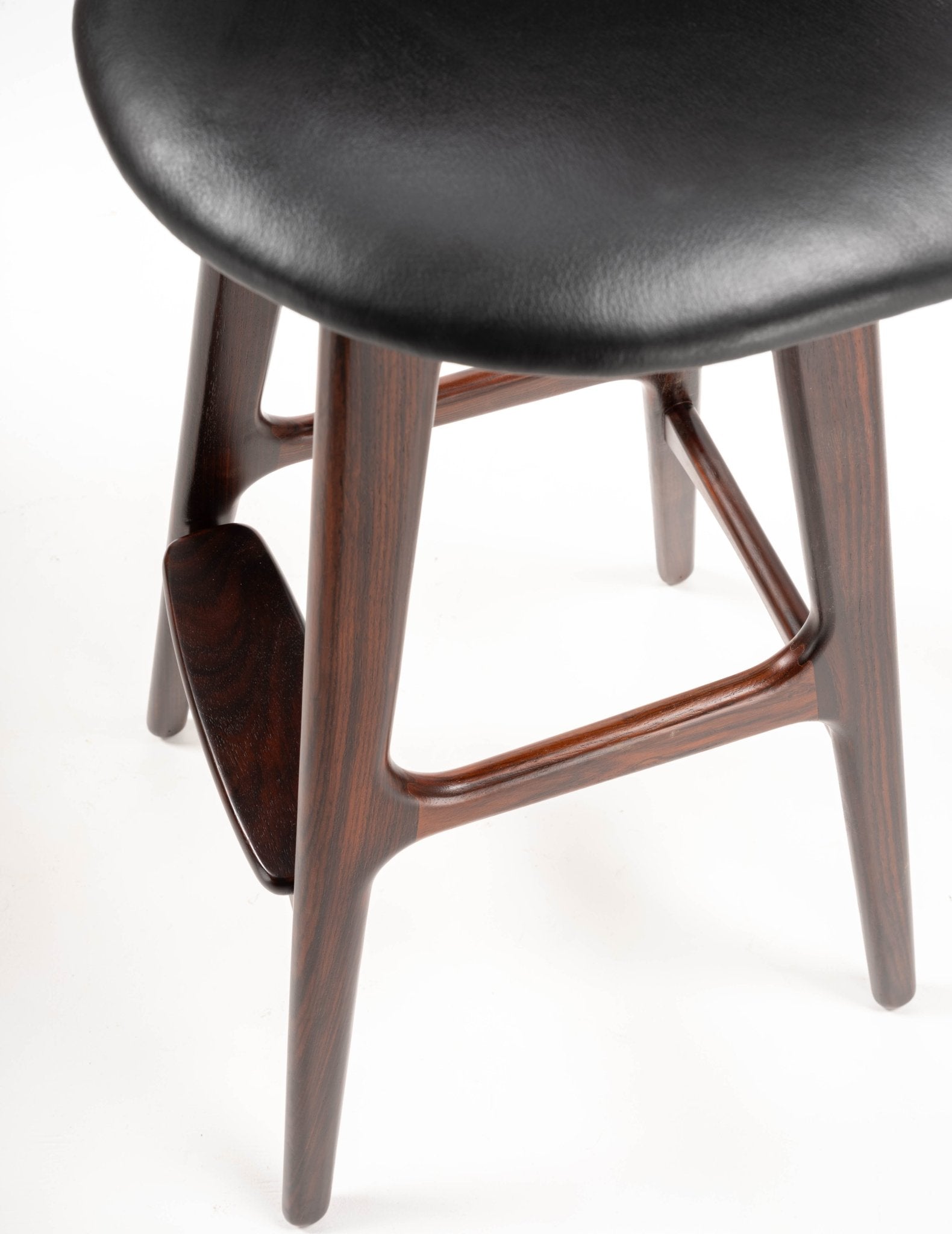 Close-up of mid-century modern Erik Buch bar stool with rosewood frame and contoured black leather seat.