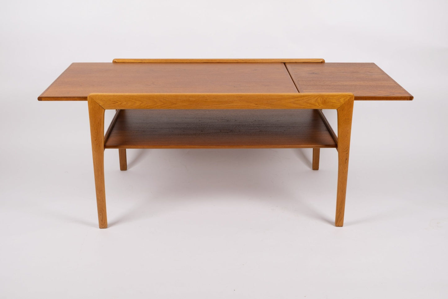 Mid-century modern expandable coffee table with tapered legs, sliding top, and lower shelf in warm wood finish