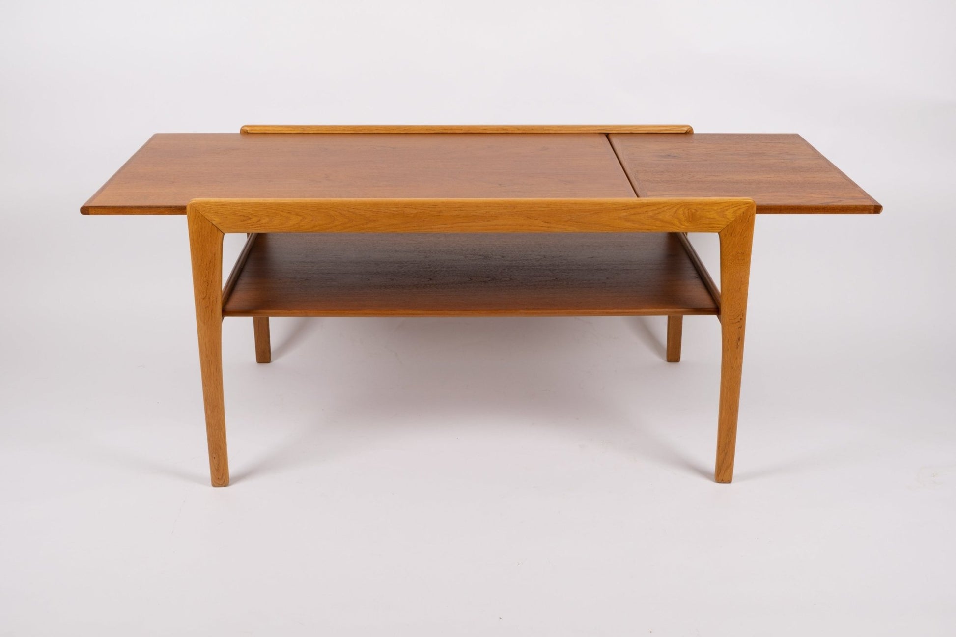 Mid-century modern expandable coffee table with tapered legs, sliding top, and lower shelf in warm wood finish