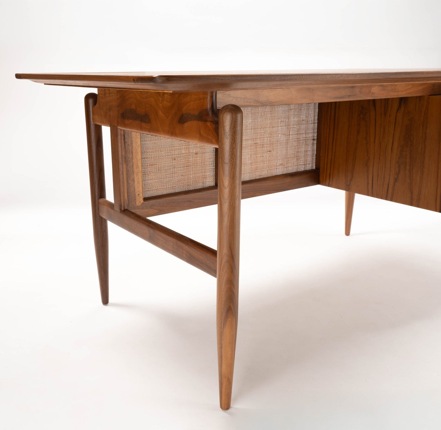 Mid-century modern Finn Juhl executive desk in walnut with cane detailing and tapered legs on white background.