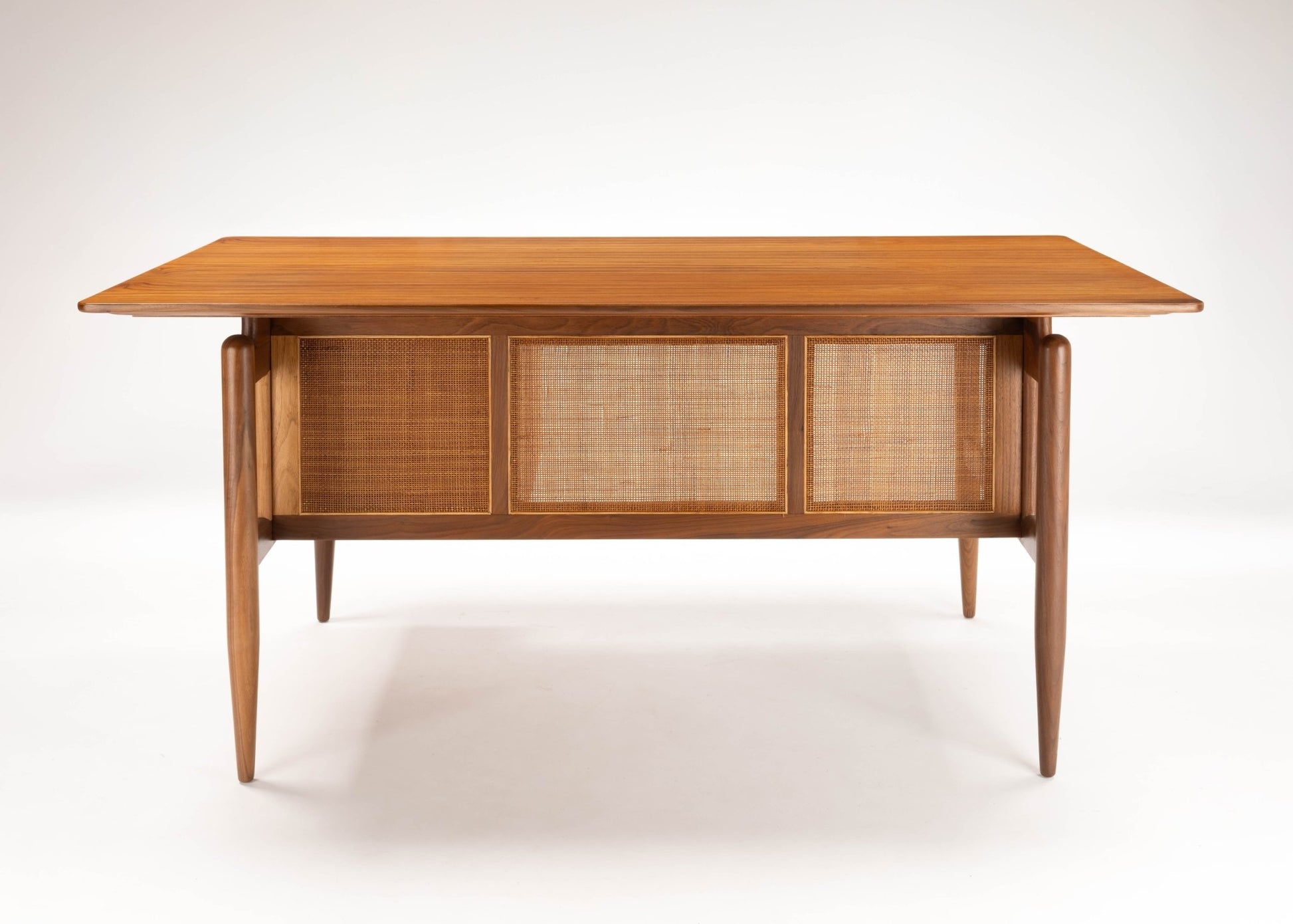 Mid-century modern Finn Juhl executive walnut desk with cane paneling and tapered legs on white background.