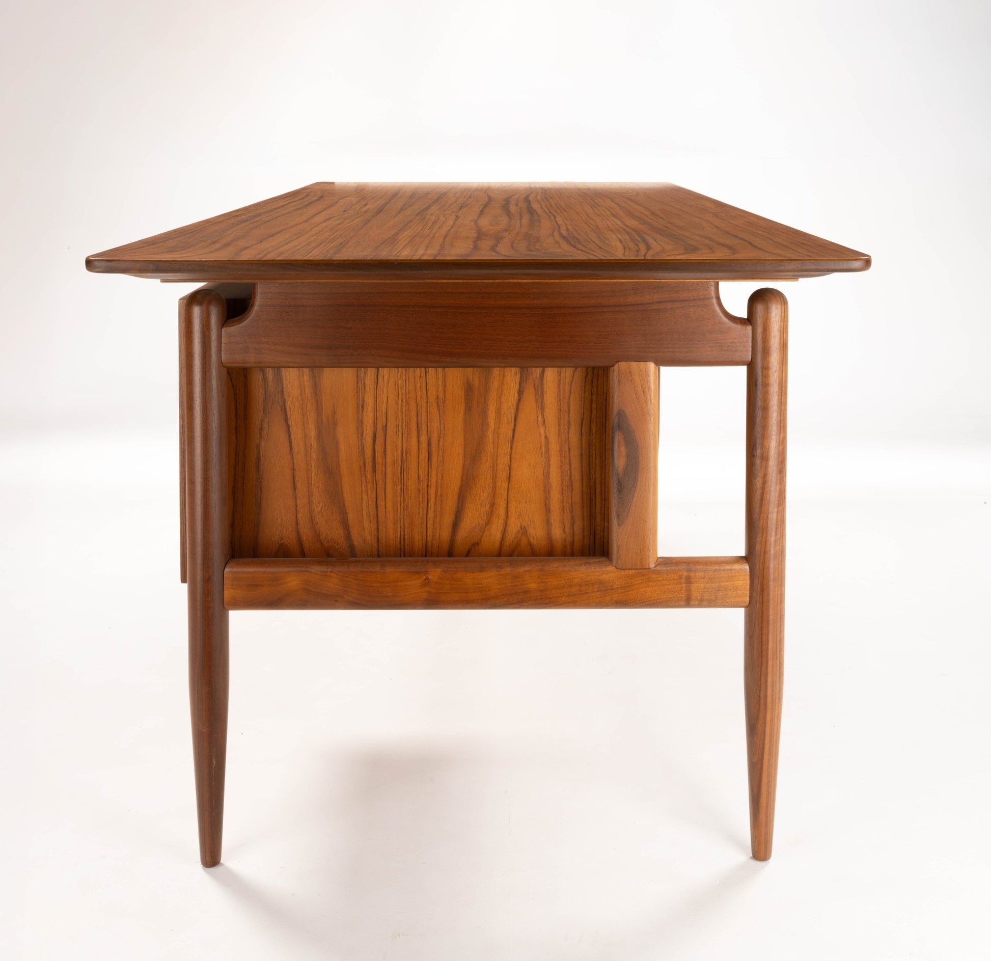 Mid-century modern walnut executive desk with tapered legs and solid panel detailing, photographed from the front