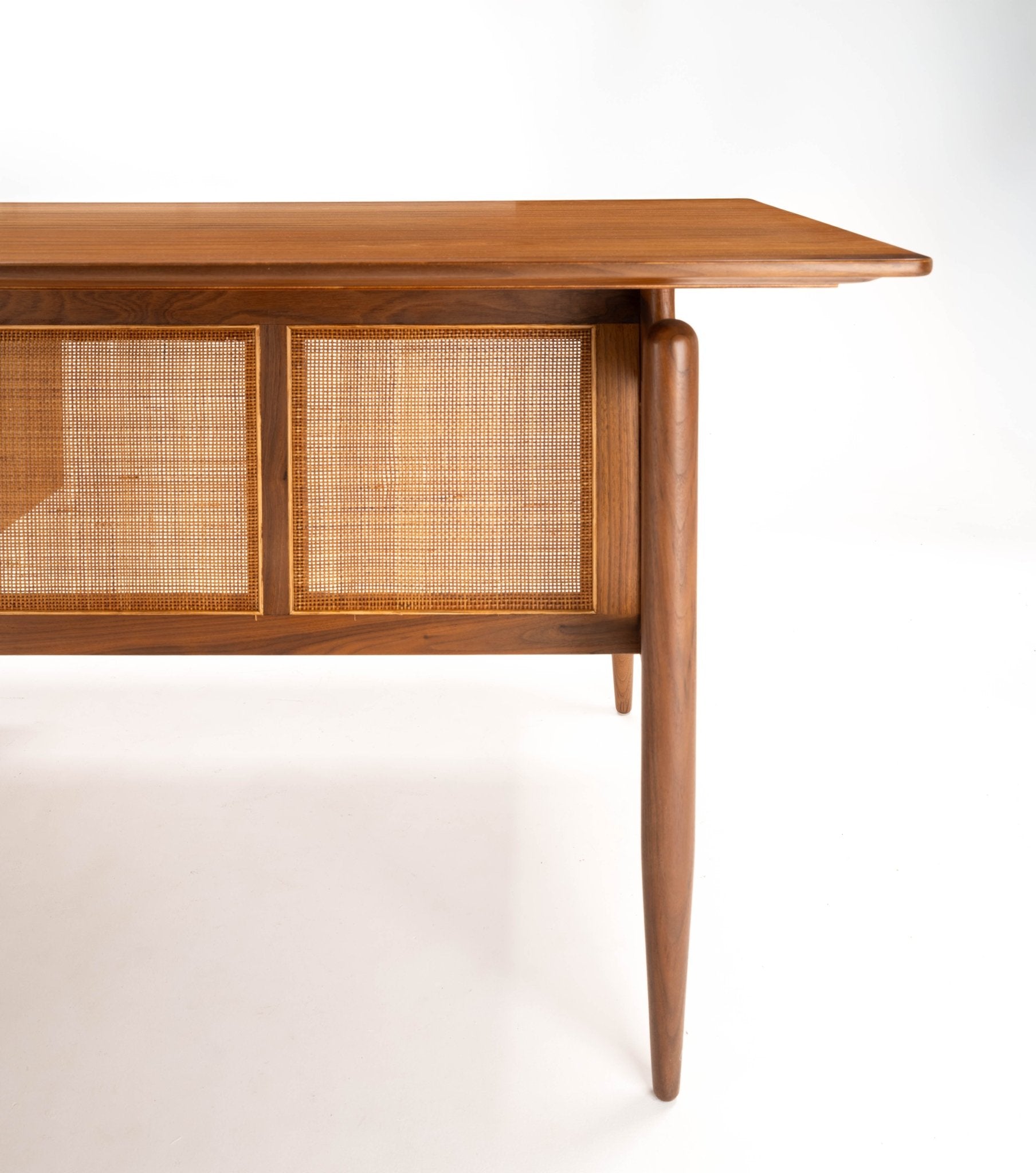 Mid-century modern Finn Juhl executive desk in walnut with cane paneling and tapered legs on white background.