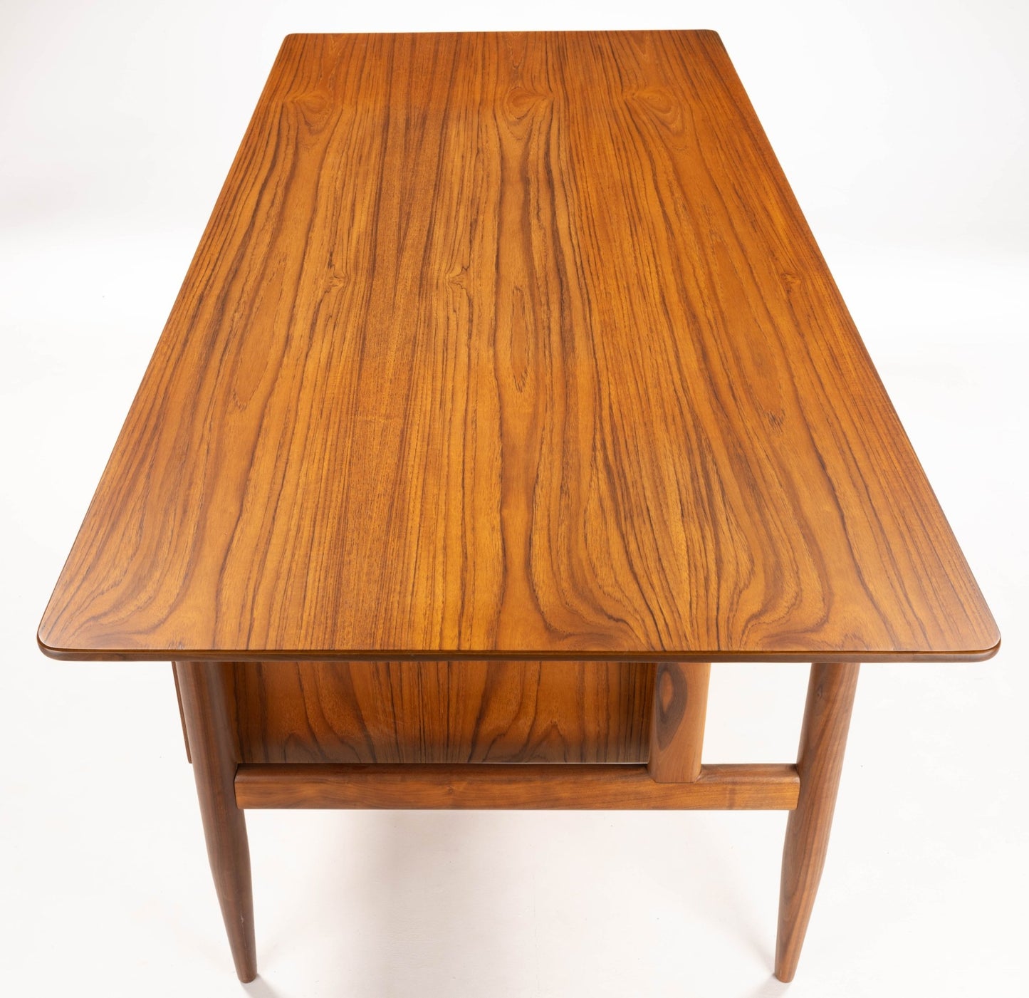 Mid-century modern walnut executive desk with sleek rectangular top and tapered legs, showcasing wood grain detail.