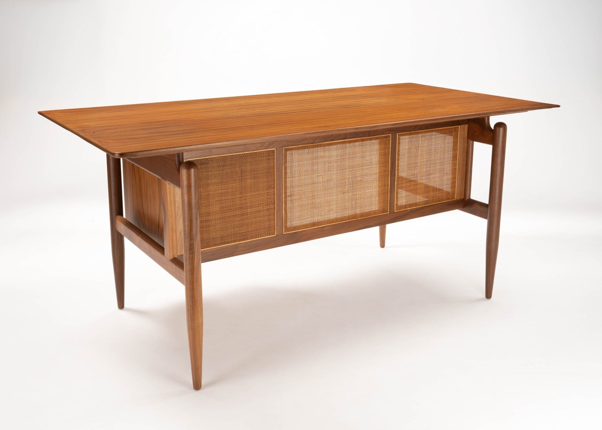 Mid-century modern Finn Juhl walnut executive desk with cane panels and tapered legs on white background.