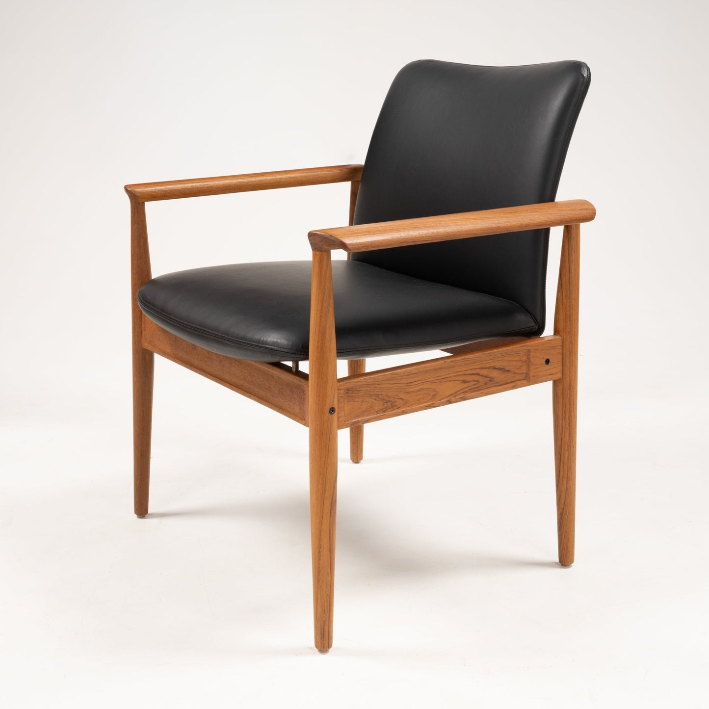 Finn Juhl Model 209 chair with teak frame, tapered legs, and black leather cushioned seat and backrest on white background