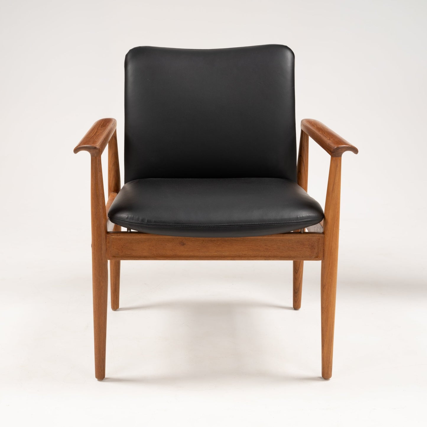 Finn Juhl Model 209 chair with teak frame, slim tapered arms, and black leather seat and backrest viewed from front