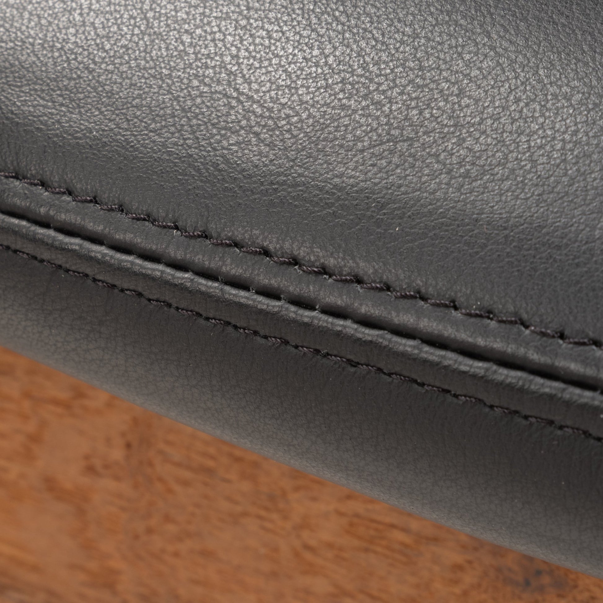 Close-up of meticulous stitching on black leather upholstery and warm teak wood frame of Finn Juhl Model 209 chair