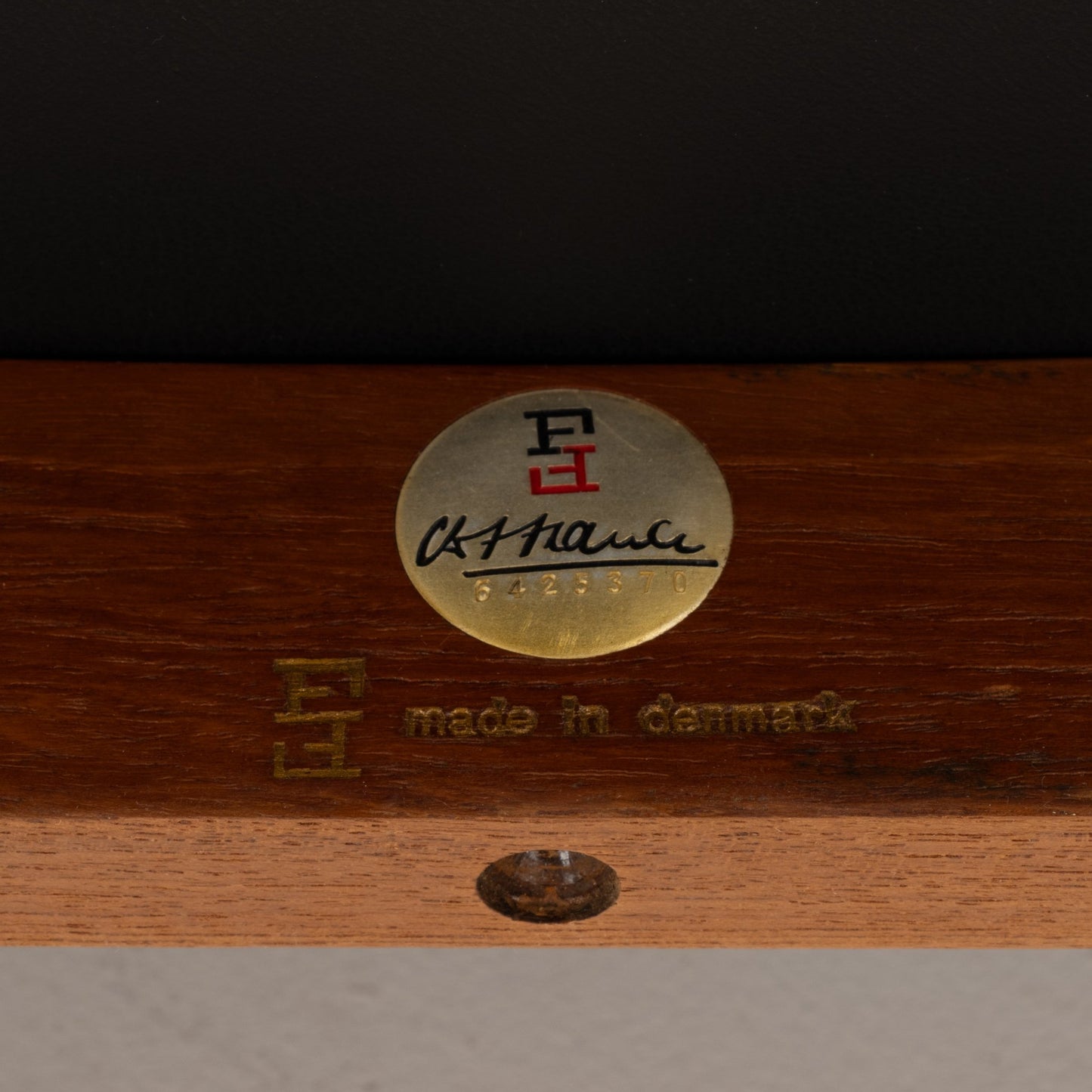 Close-up of brass authenticity badge and stamped logo on hand-finished teak frame of Finn Juhl Model 209 chair