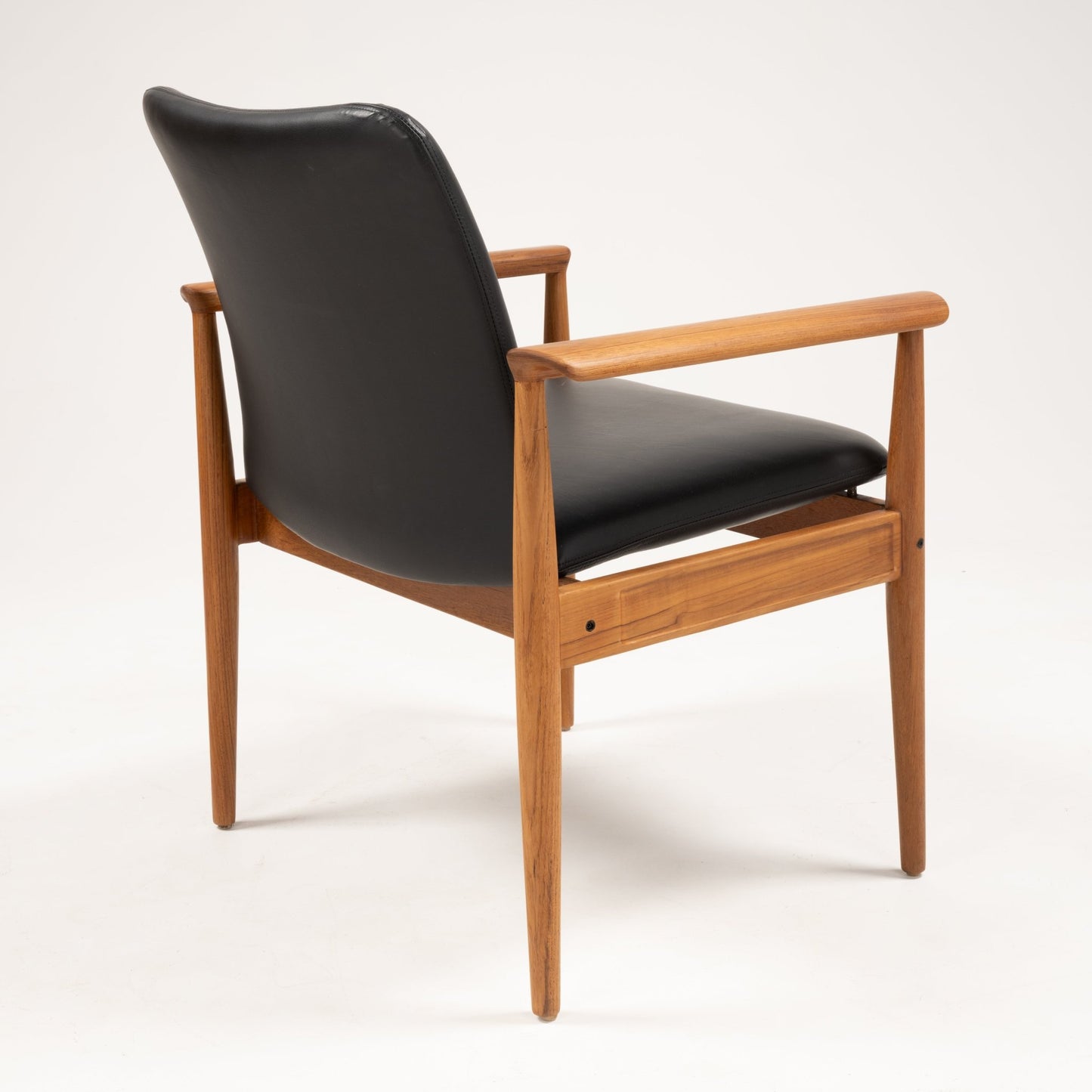 Rear view of Finn Juhl Model 209 "Diplomat" chair with teak frame and black leather upholstery on white background
