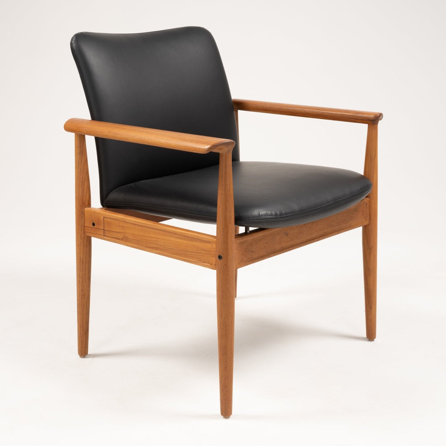 Finn Juhl Model 209 "Diplomat" chair with teak frame, tapered legs, and black leather seat and backrest on white background