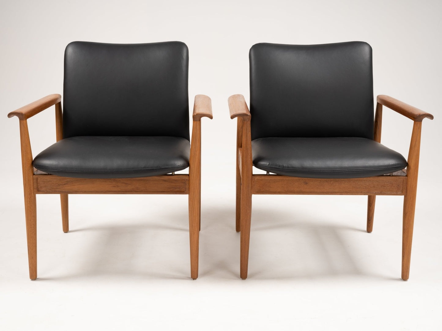 Pair of Finn Juhl Model 209 chairs with teak frames and black leather cushions, featuring slender tapered legs and armrests