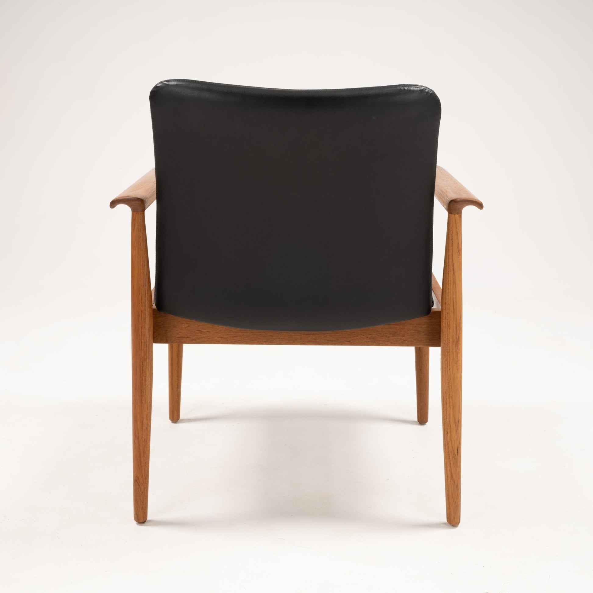 Back view of Finn Juhl Model 209 chair showcasing teak frame with slim tapered legs and black leather backrest