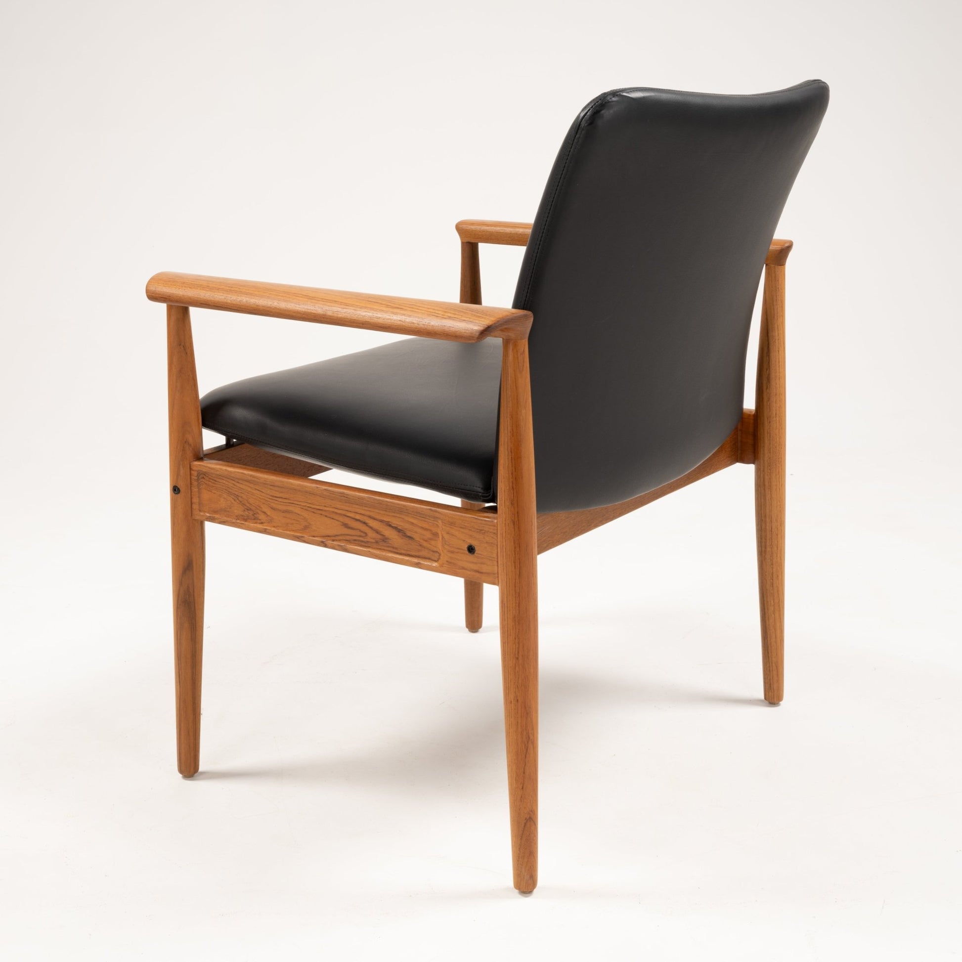Rear angle of Finn Juhl Model 209 "Diplomat" chair featuring teak frame and black leather upholstery on white background