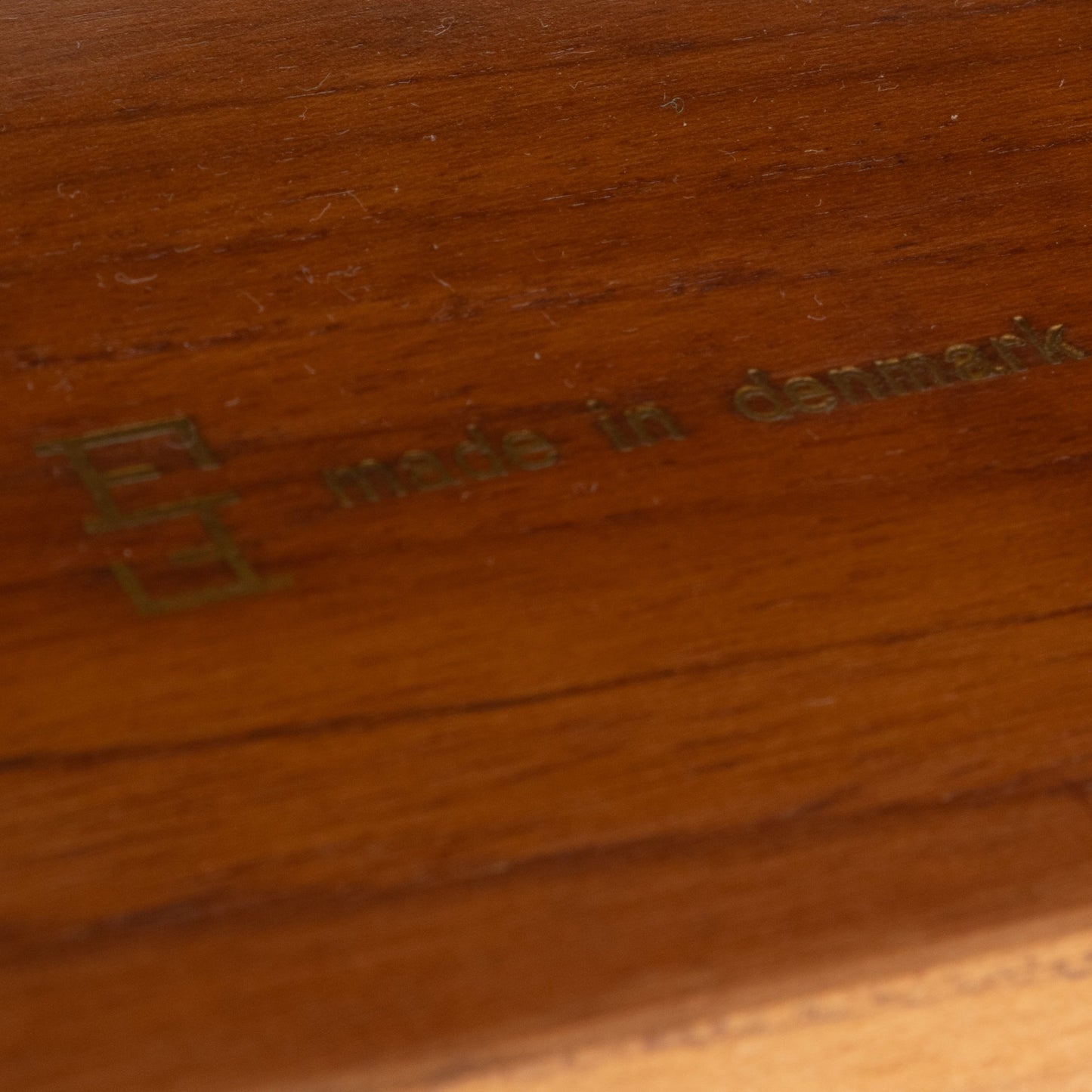 Close-up of brass "made in Denmark" stamp on smooth, hand-finished teak surface of Finn Juhl Model 209 chair