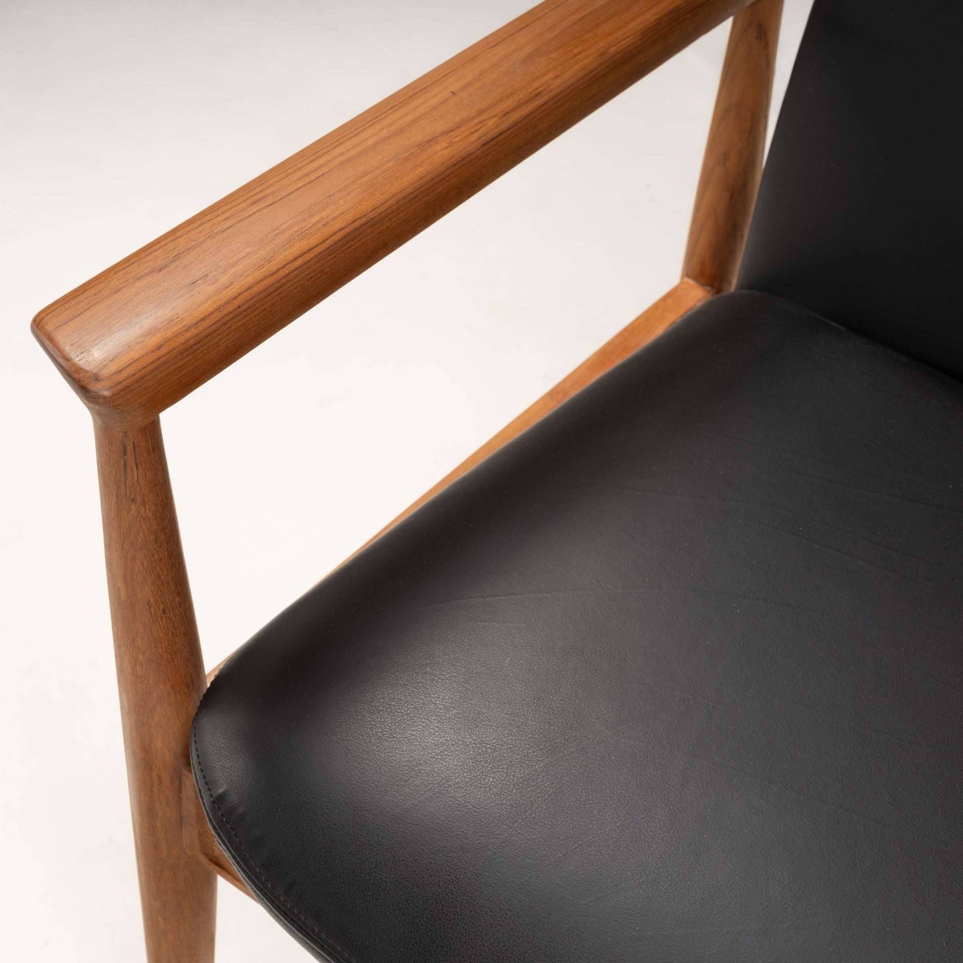 Close-up of smooth teak armrest and black leather seat cushion on a Finn Juhl Model 209 "Diplomat" chair