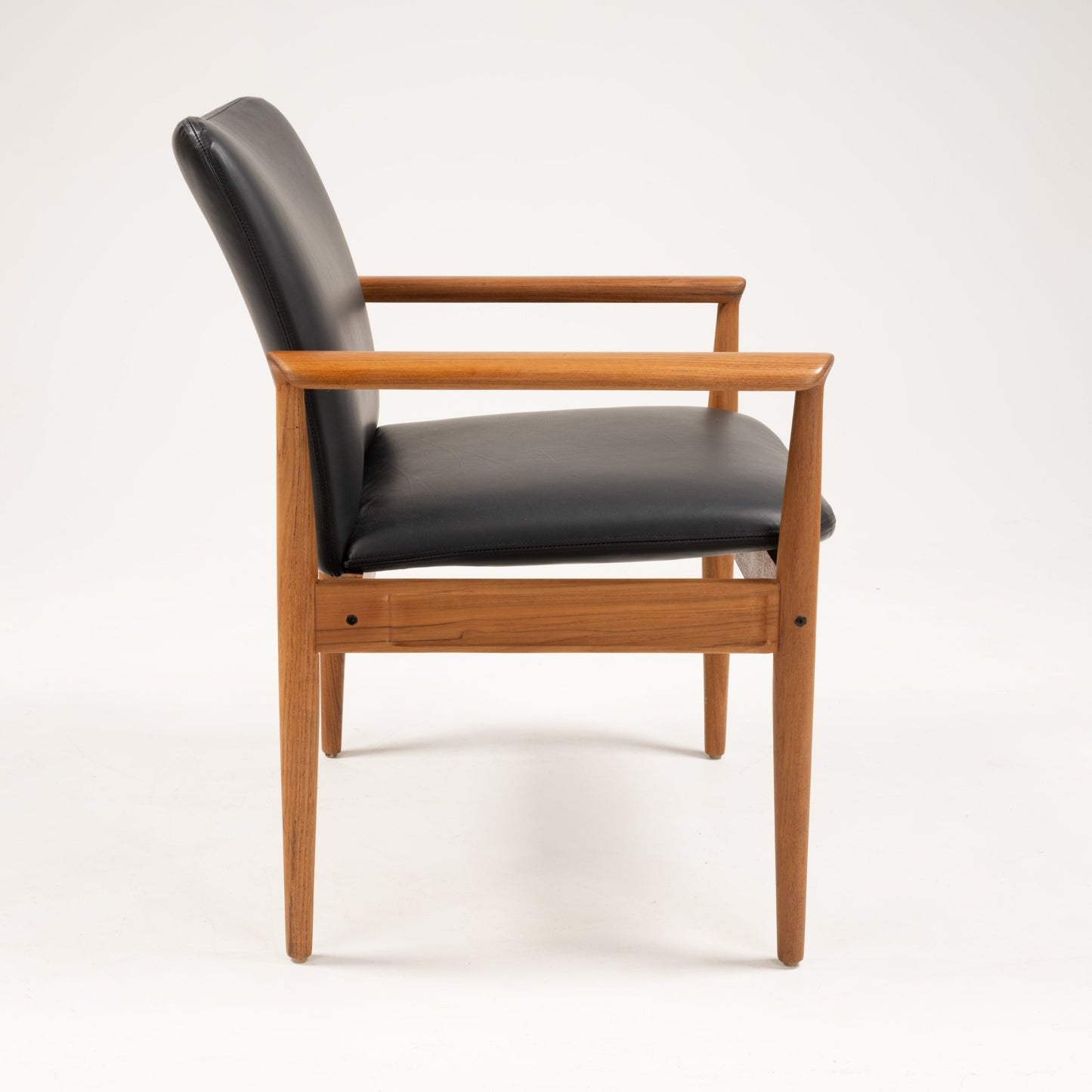 Side view of Finn Juhl Model 209 chair with teak frame and black leather seat and backrest on white background