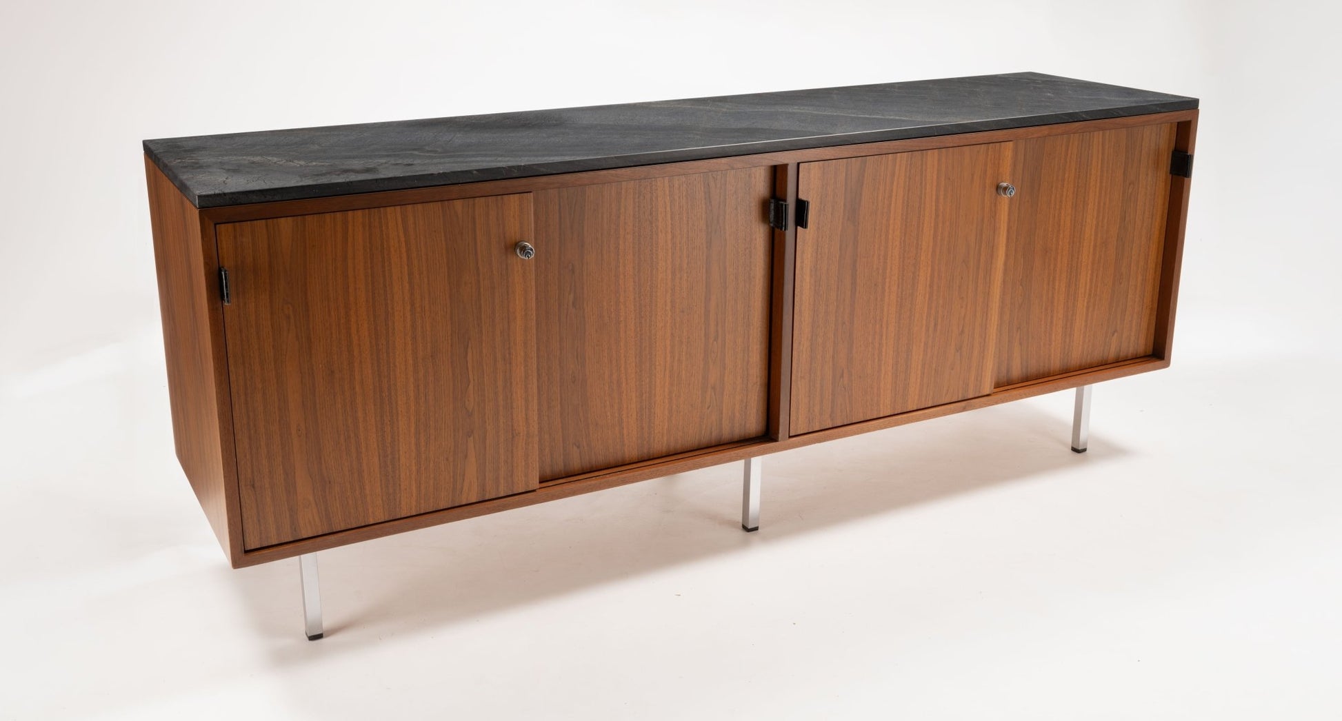 Mid-century walnut credenza with four locking sliding doors, leather pulls, and black marble top on polished metal legs.